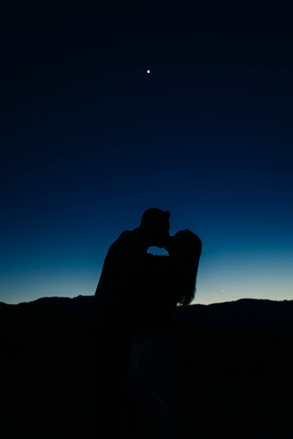 A couple kisses in front of a starry dusk sky.