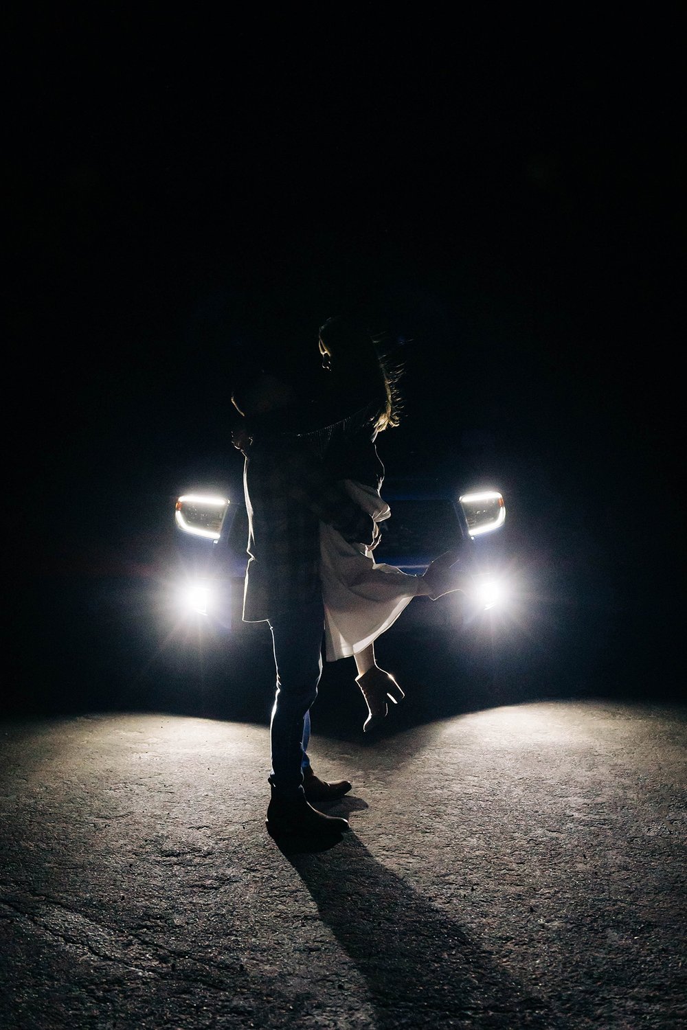 A man picks up a woman in front of the headlights of their truck.