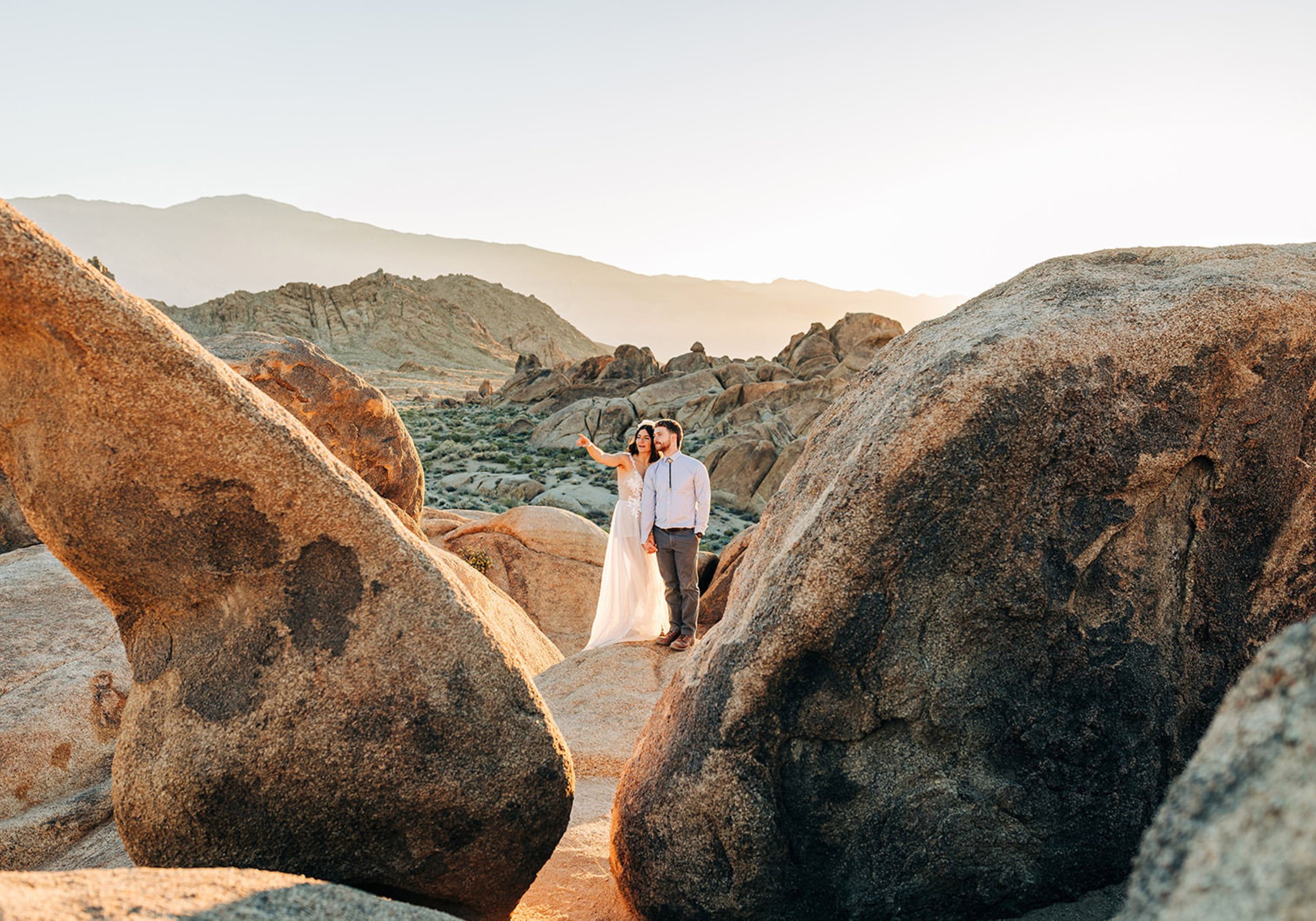 A couple standing on a rock holding hands as one points out into the distance. 