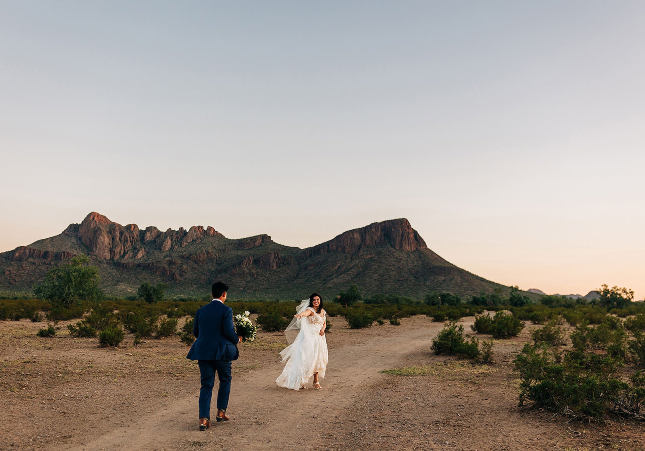 A newlywed couple walking down a flat hiking path outdoors.