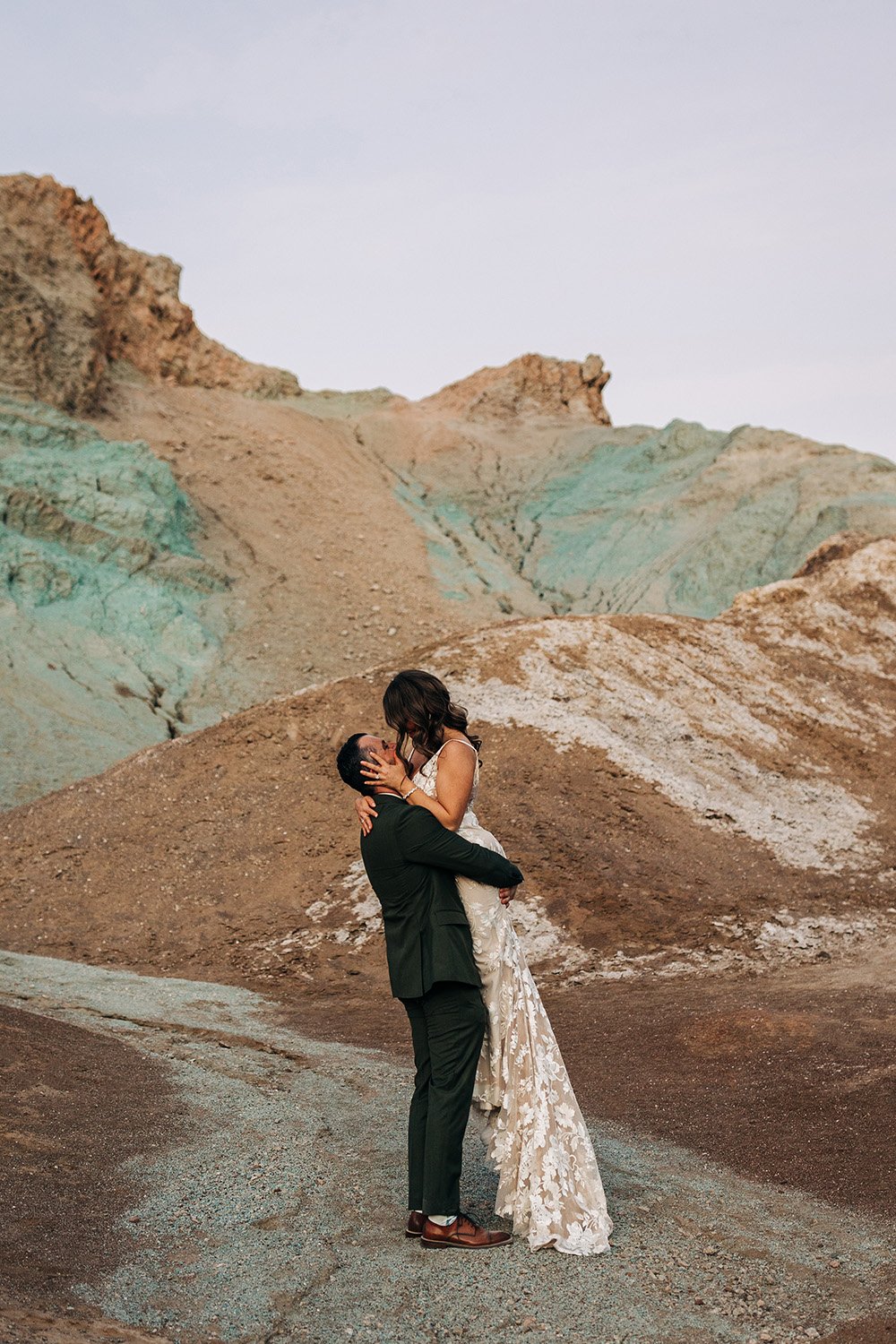 A man picks up his wife in a wedding dress in the colorful hills of Death Valley. 