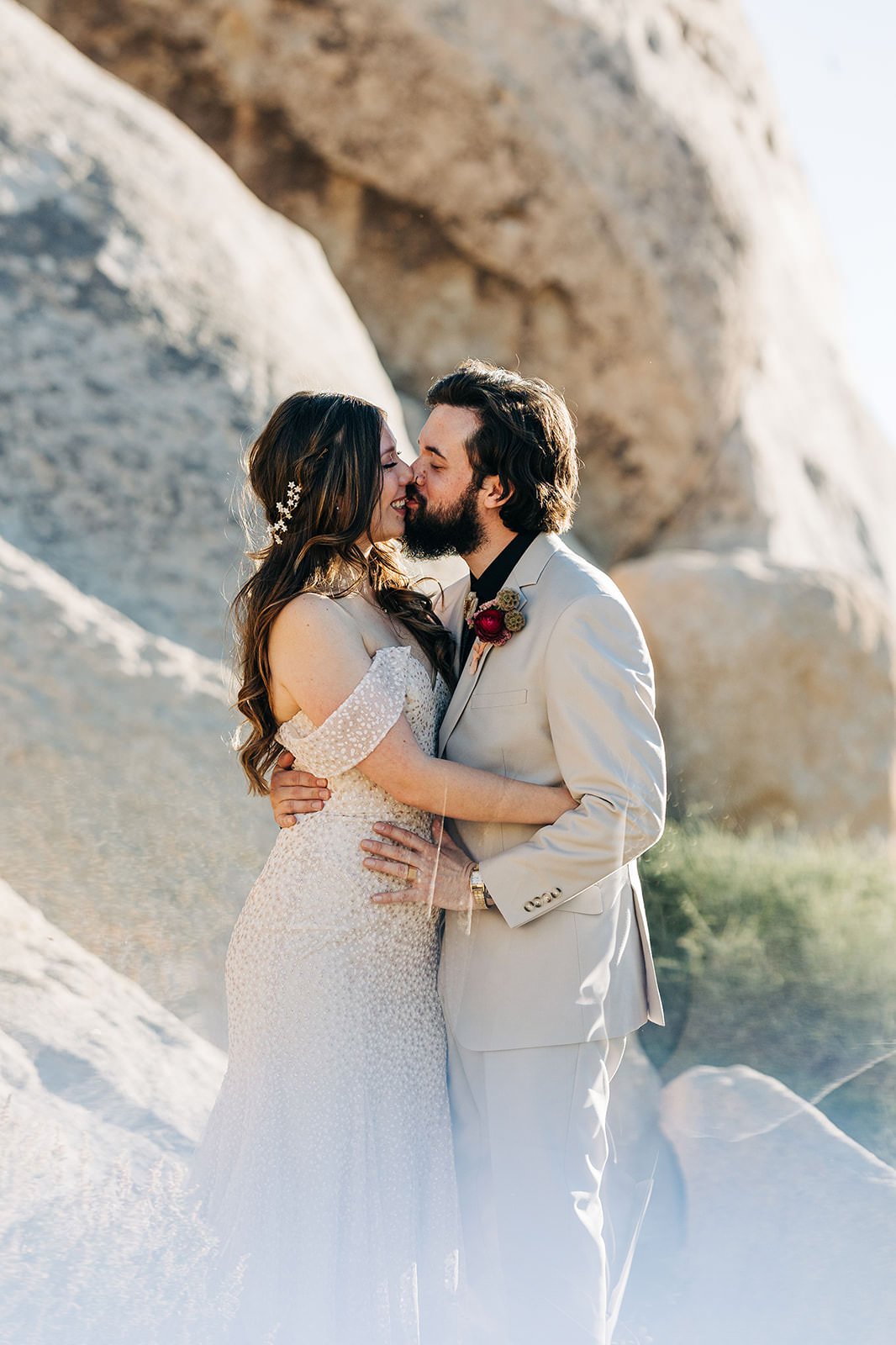 A newlywed couple kissing in front of tan rocks. 
