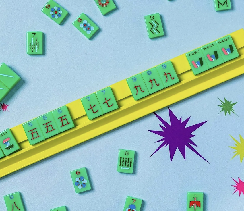 Mahjong tiles arranged on a yellow rack and scattered on a light blue surface with colorful starburst and halo designs.