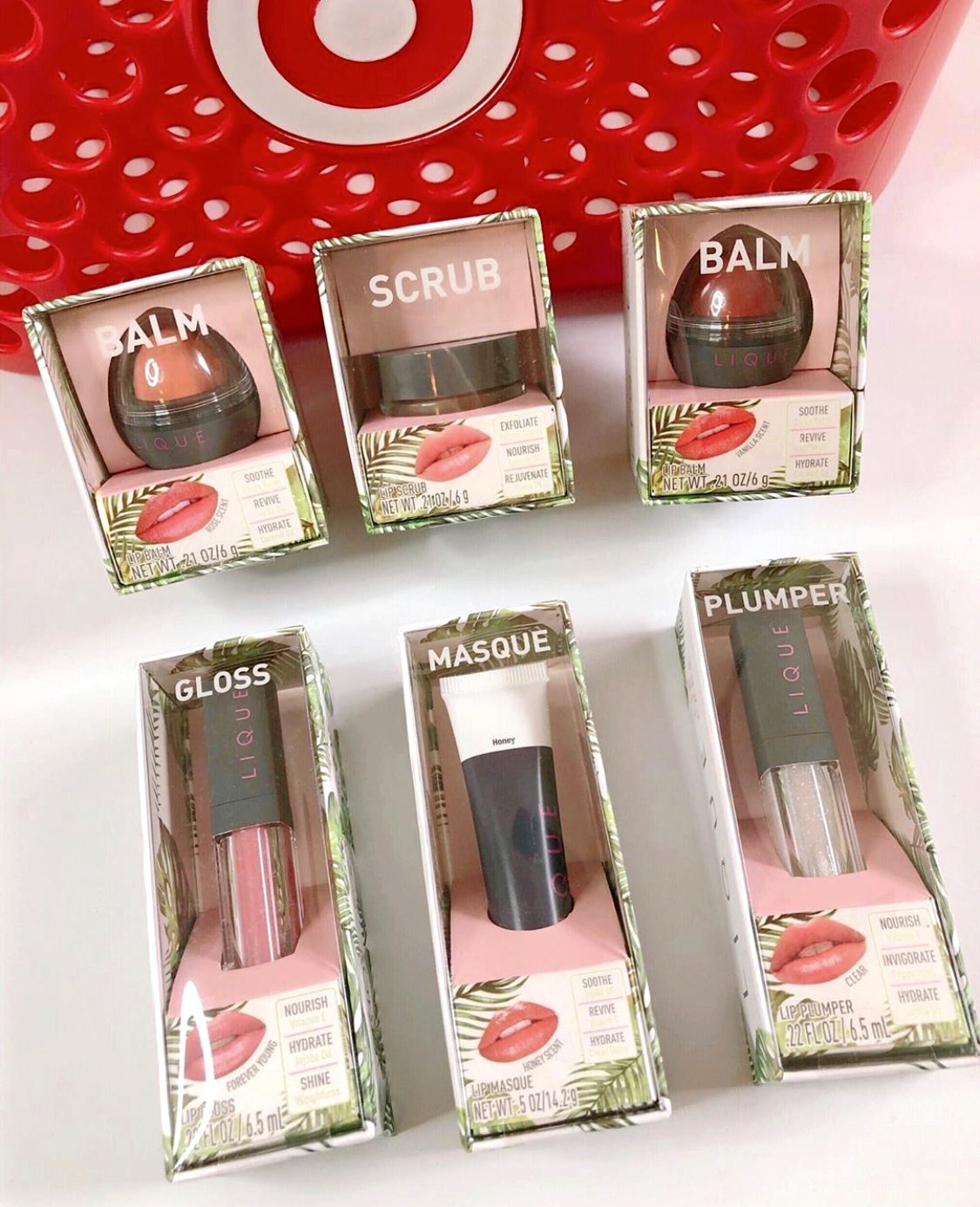 Assorted lip care products in boxes, including balm, scrub, gloss, masque, and plumper, displayed in front of a red Target shopping basket with a bullseye logo.