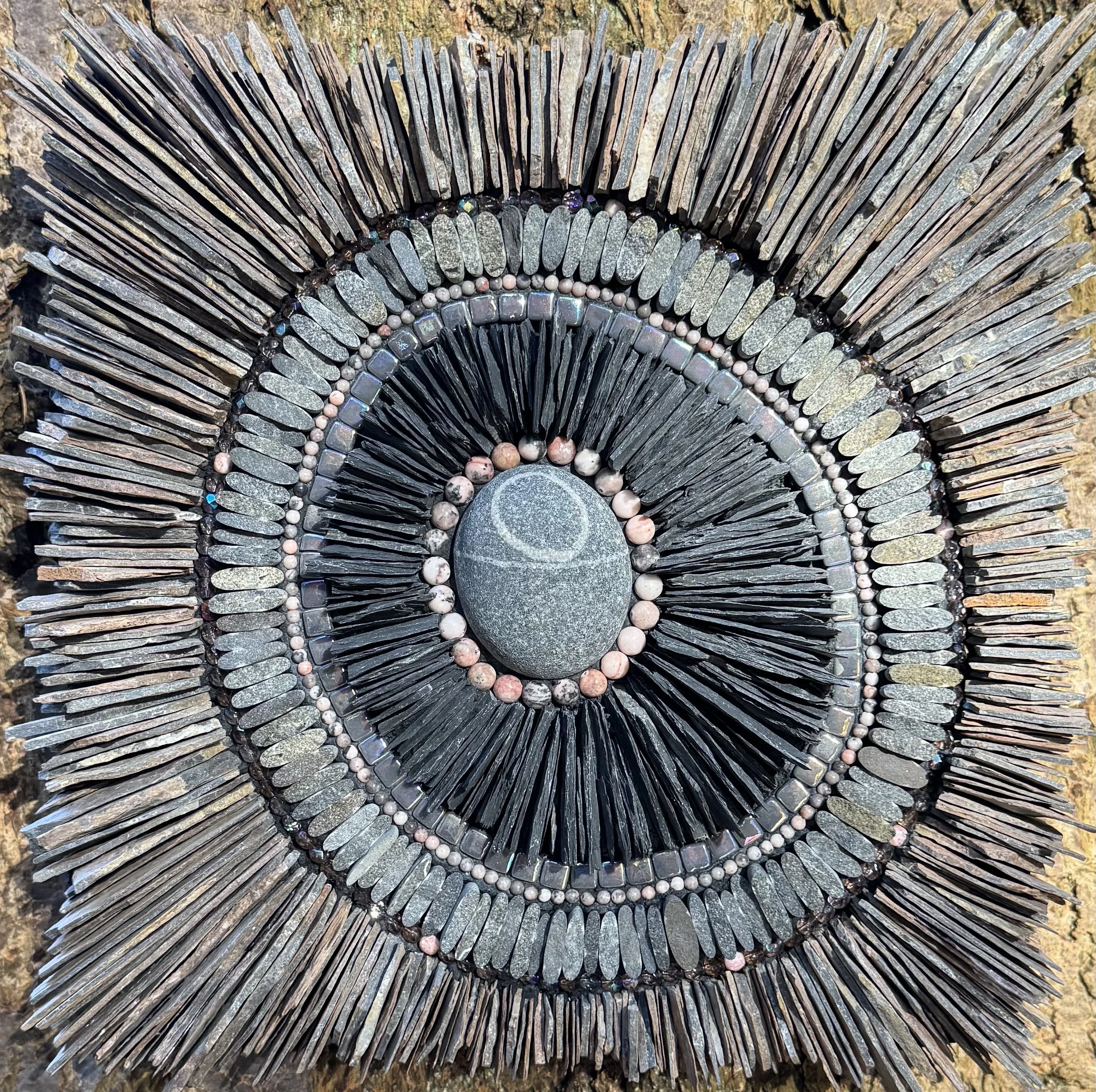 
"Halo" - Beach cobble of the metamorphic rock, quartzite. Black slate from repurposed roofing tiles, pink/grey slate scavenged from eastern Nevada, beach pebbles, rhodonite beads, glass beads and tiles. 12" x 12". Available.
