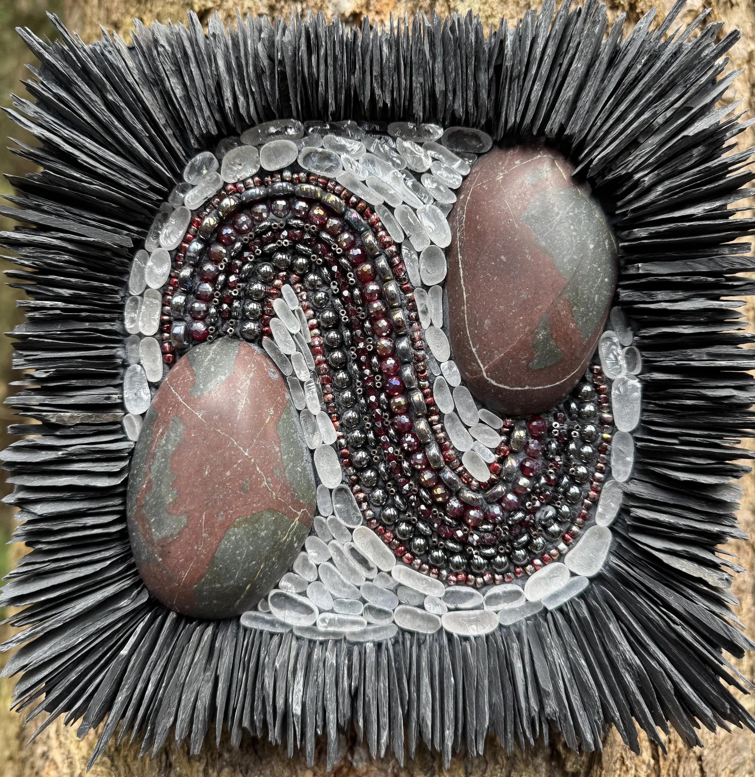 "In Vein" - Split and polished cobble of hydrothermally altered basalt displaying oxidation and quartz veining. Beach glass, glass and metal beads, and slate. 8"x8" On a wood substrate with pieces embedded in thinset. Available.
