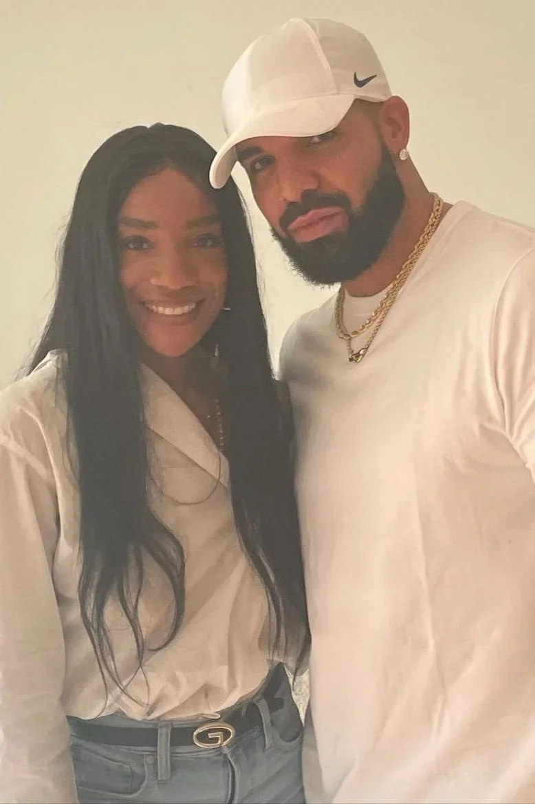 A woman with long dark hair and a man with a beard wearing a white Nike cap and white shirt, both smiling and standing close together.