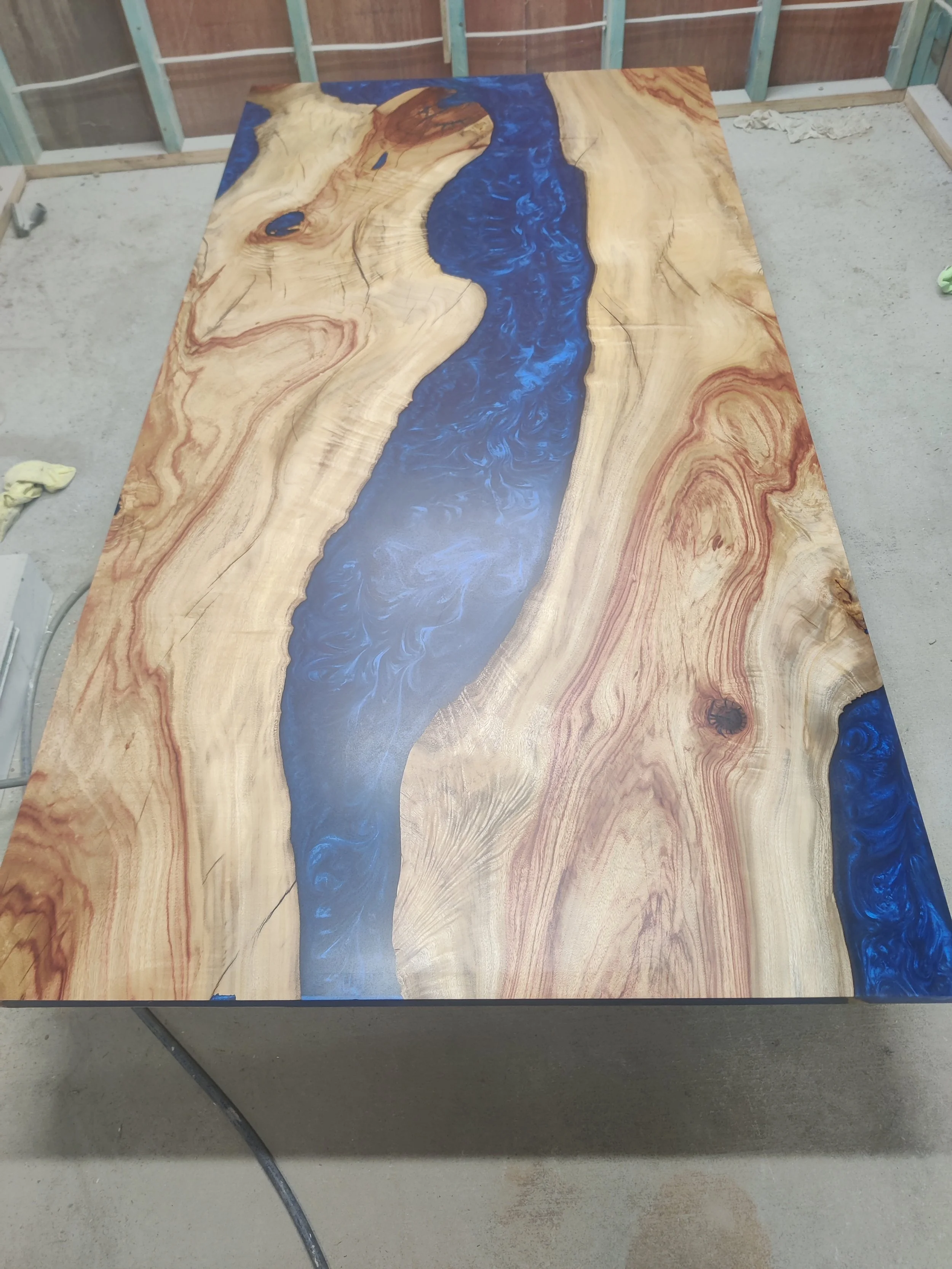 Wooden table with blue epoxy resin river feature, unfinished room.