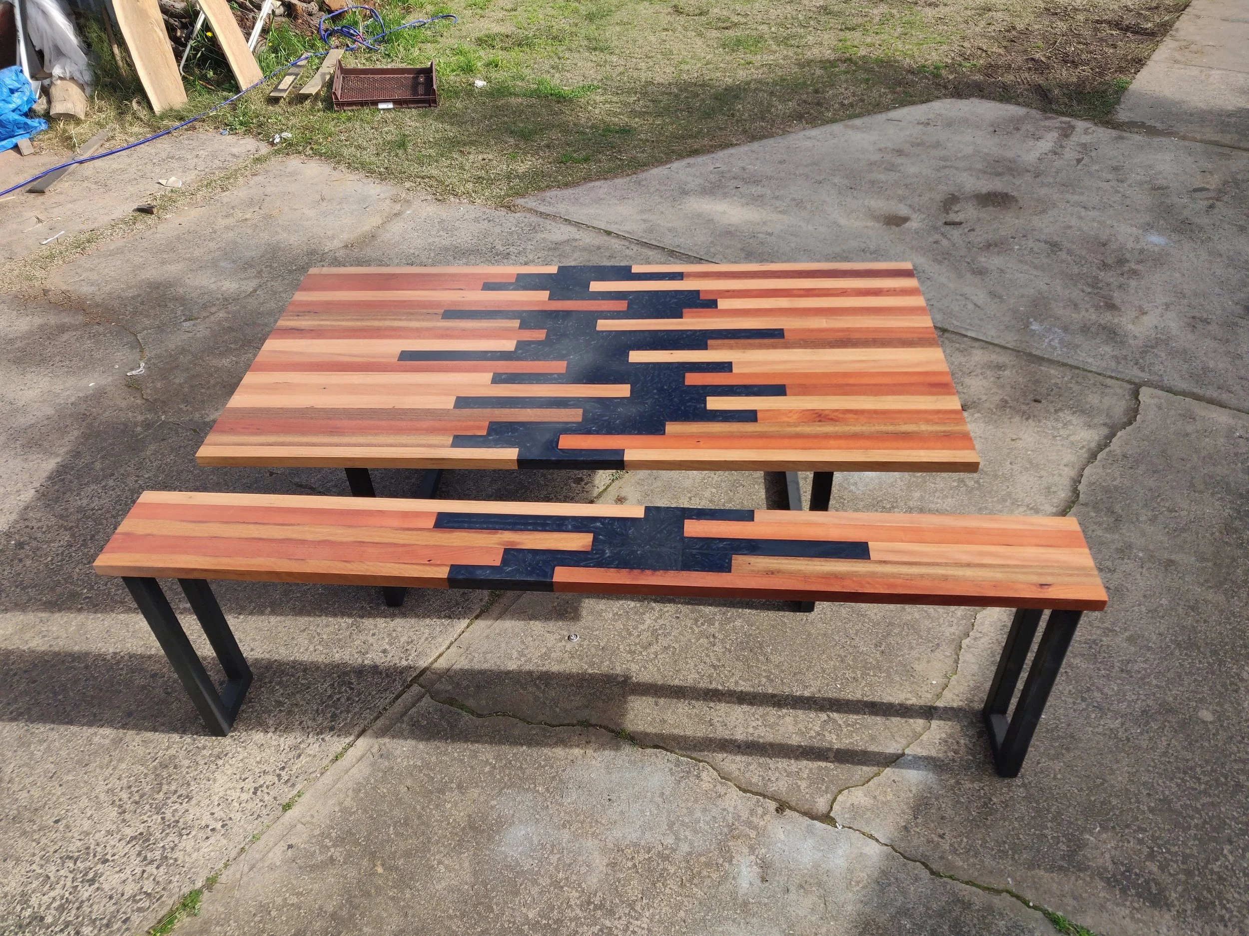 Wooden table and bench with black geometric inlay design on a concrete surface outdoors.