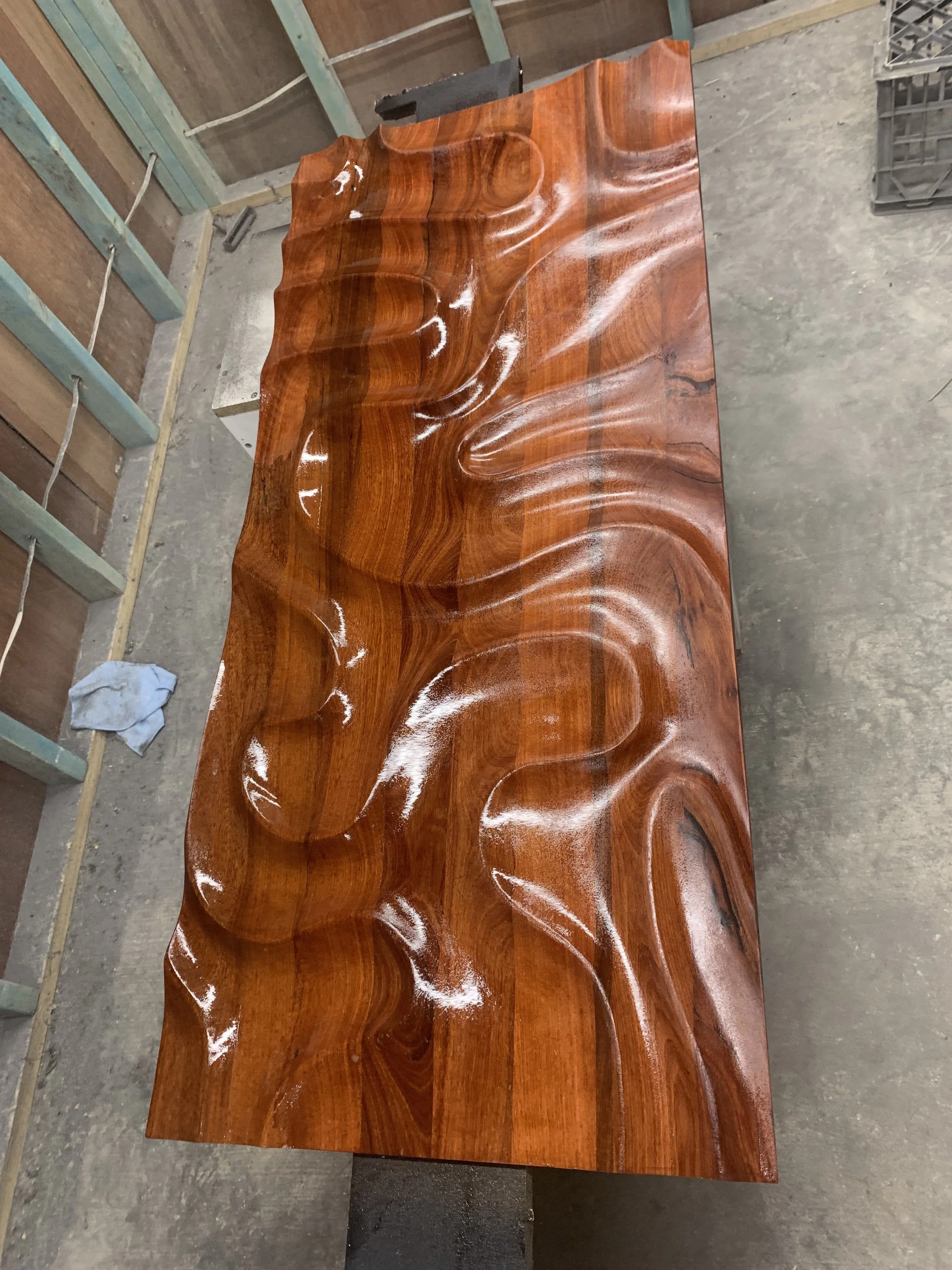 Smooth, glossy wooden table with undulating waves carved into the surface, reflecting light.