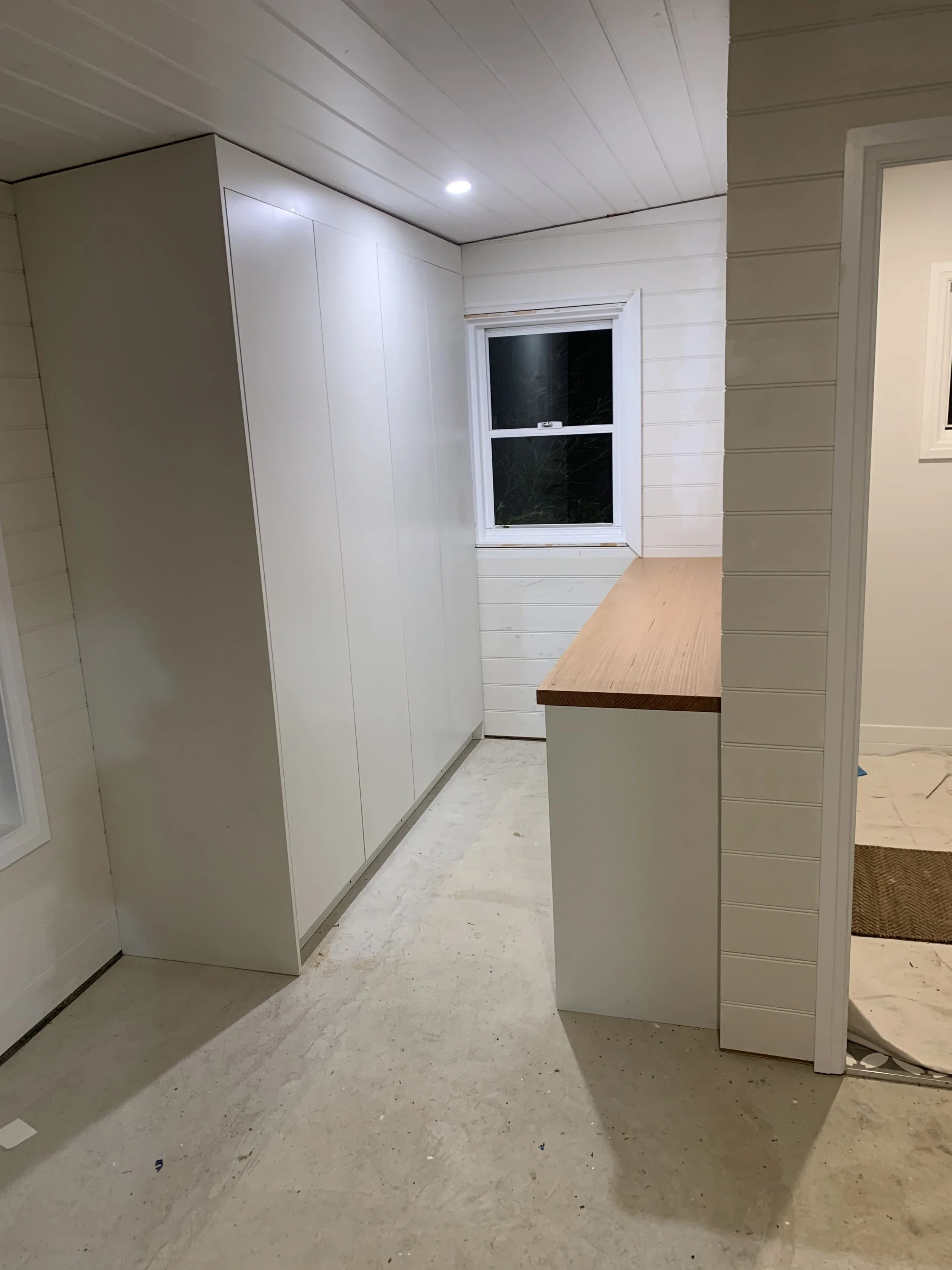 Minimalist kitchen interior with white walls, ceiling, and cabinets, featuring a wooden countertop and a window with a view outside.