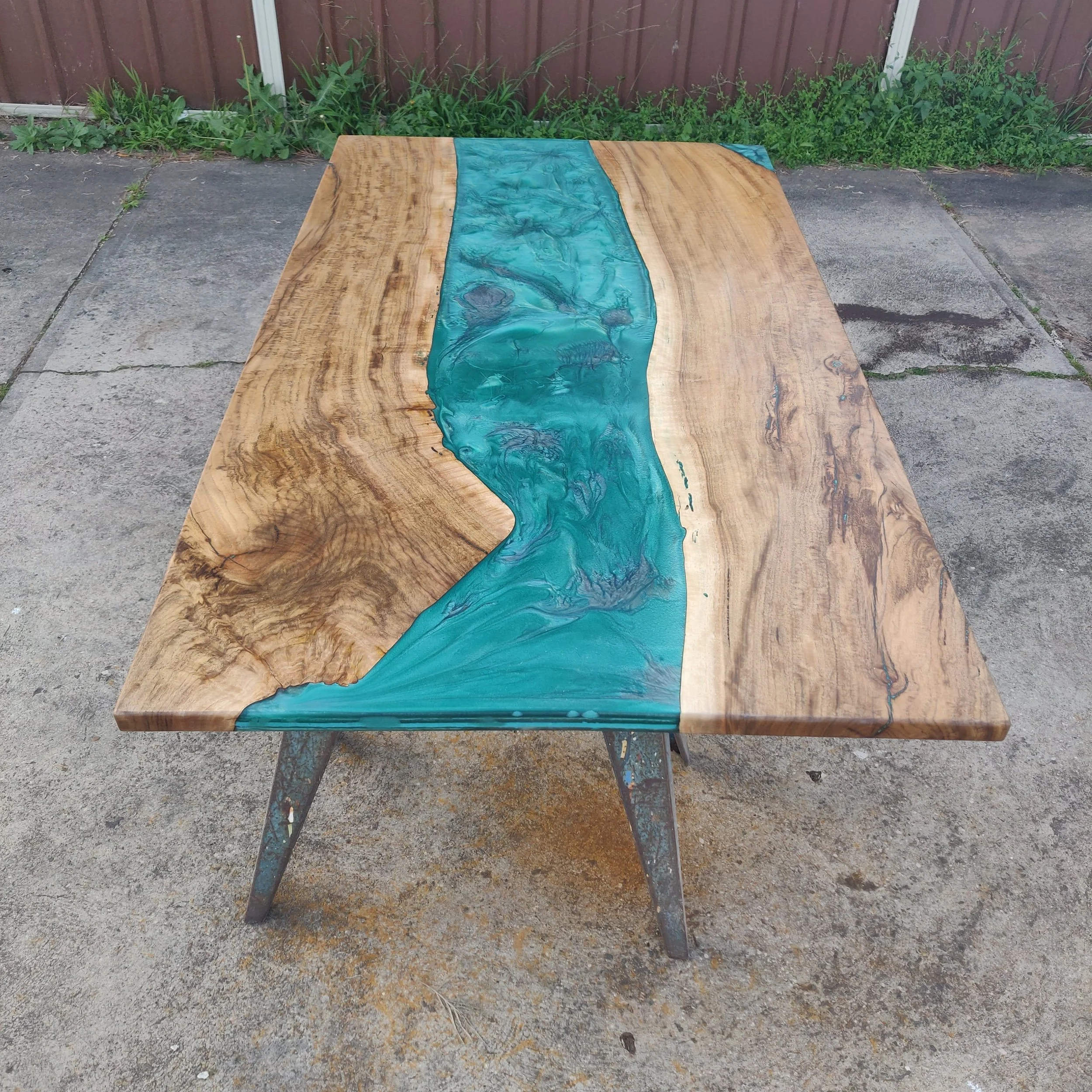 Wooden table with turquoise epoxy resin river design outdoors on concrete surface.