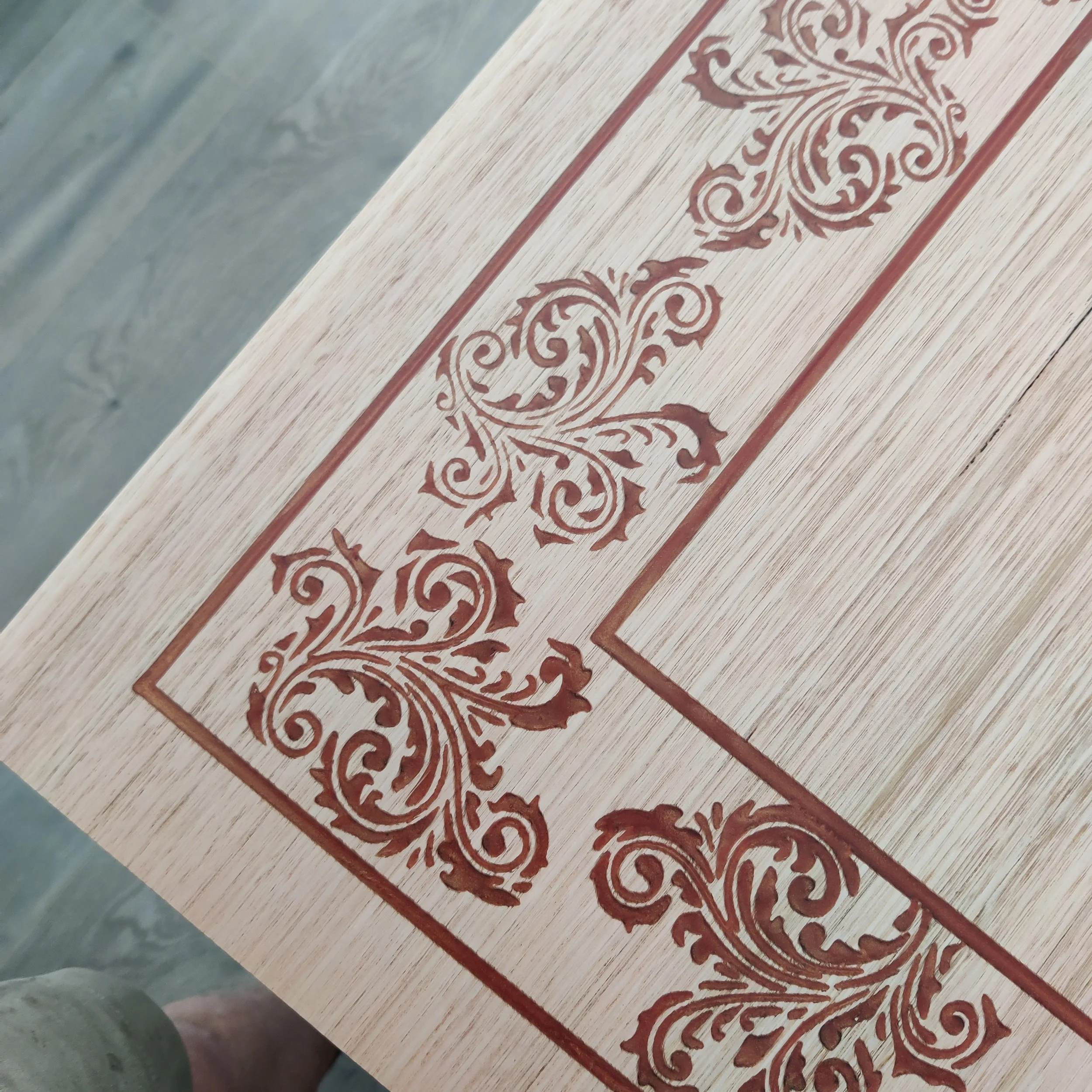 Close-up of a light wood surface with intricate red floral carvings along the edge, set against a gray background.