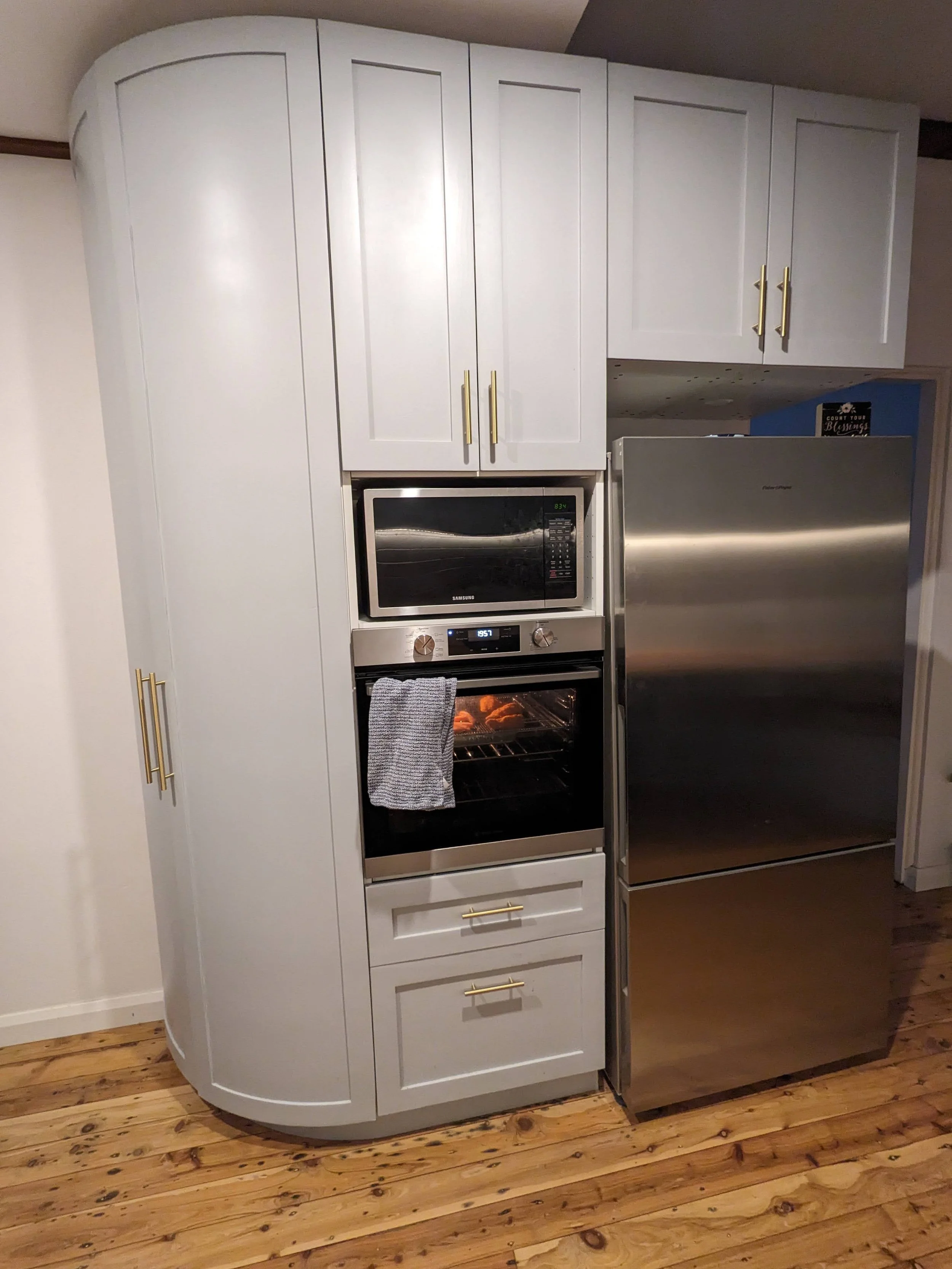 Modern kitchen with white cabinets, built-in microwave, oven, stainless steel refrigerator, and wooden floor.