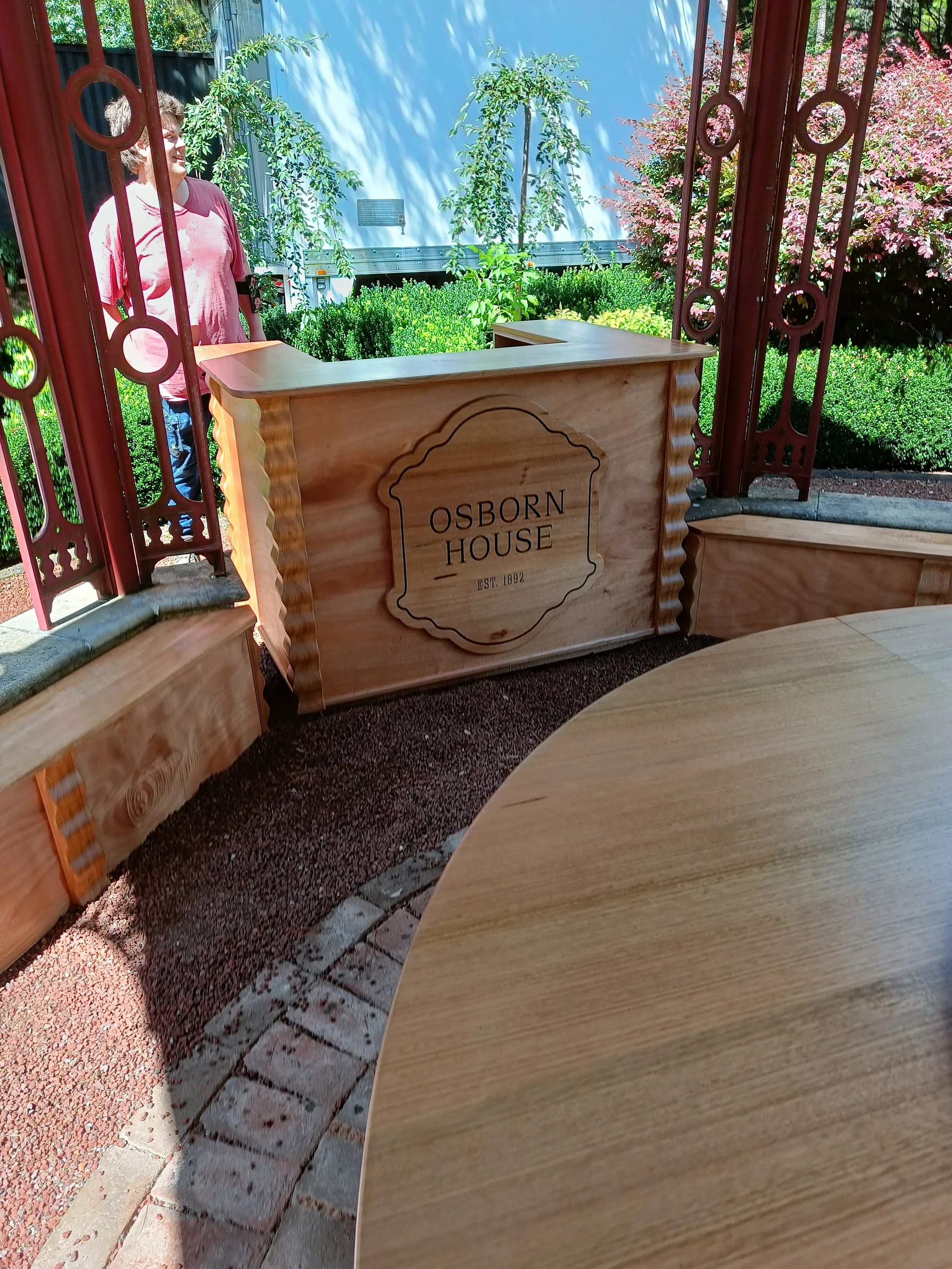 Wooden sign reading "Osborn House Est. 1892" in a garden setting, with greenery and a person in the background.