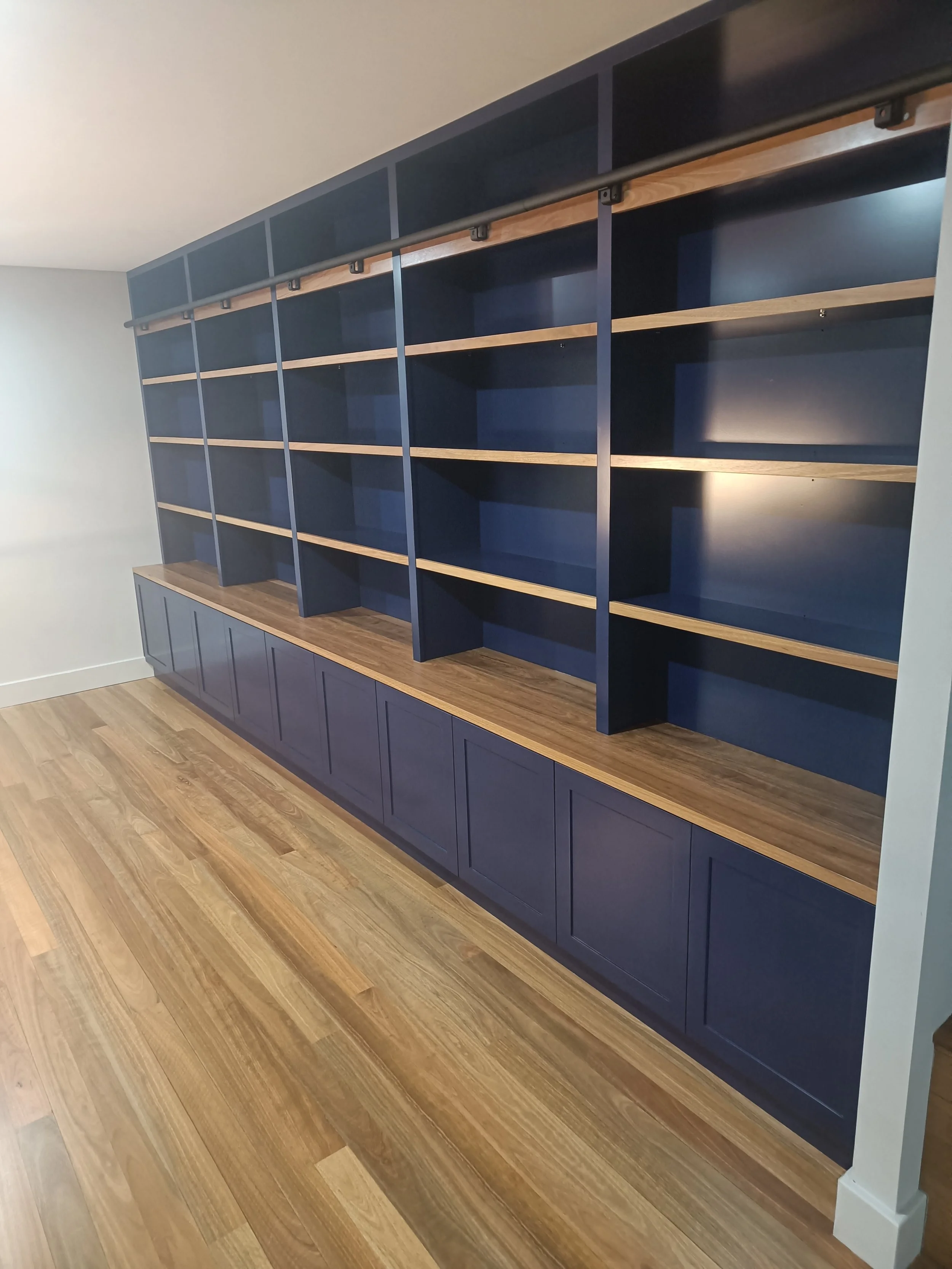 Large built-in wooden shelving unit with a navy blue finish and multiple open shelves, set against a wall with a light hardwood floor.