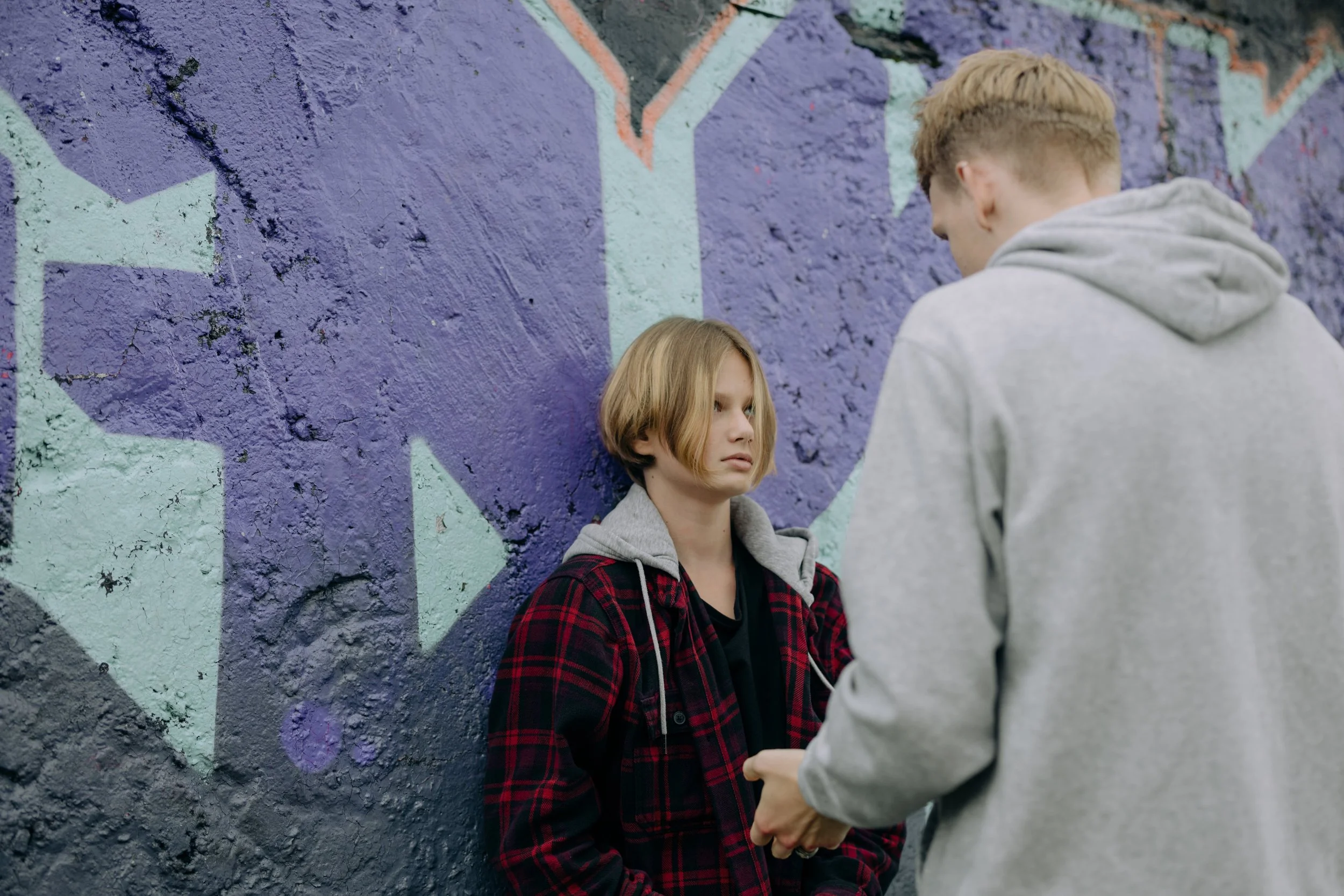 young person leaning against a wall and looking up at another person standing in front of them