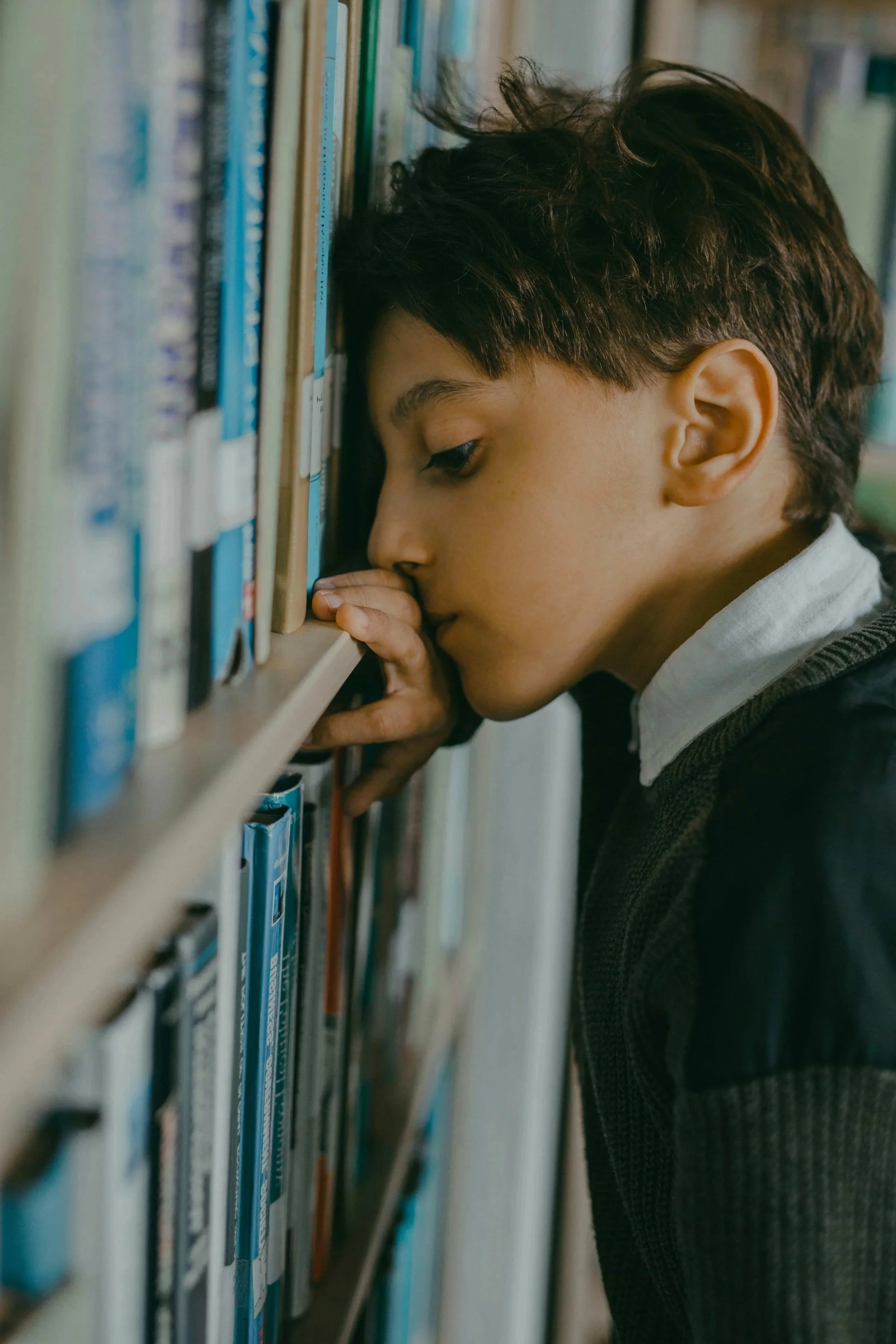young boy in school uniform leaning against a wall looking sad
