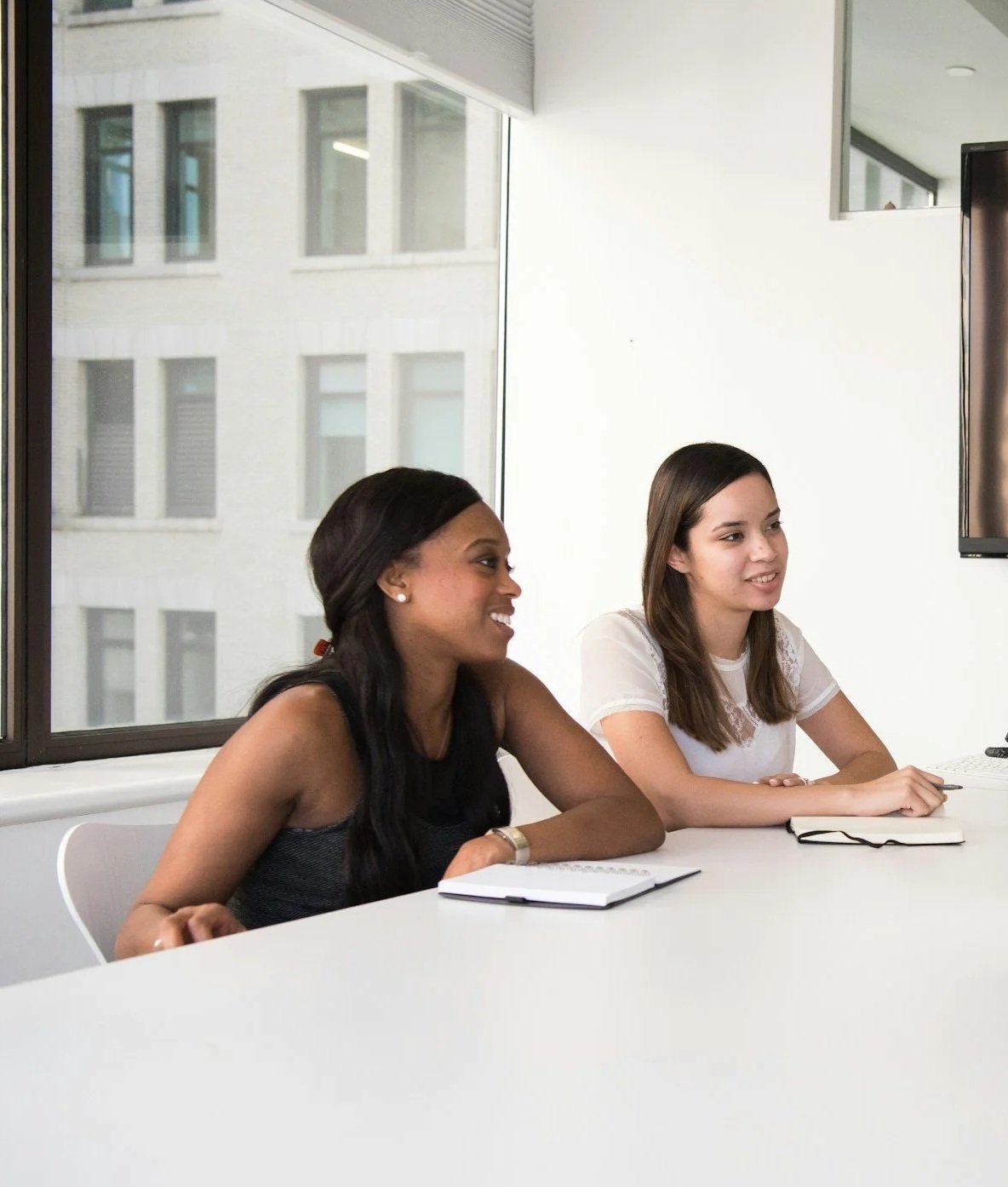 two women in a meeting sitting at a white table with window in the background