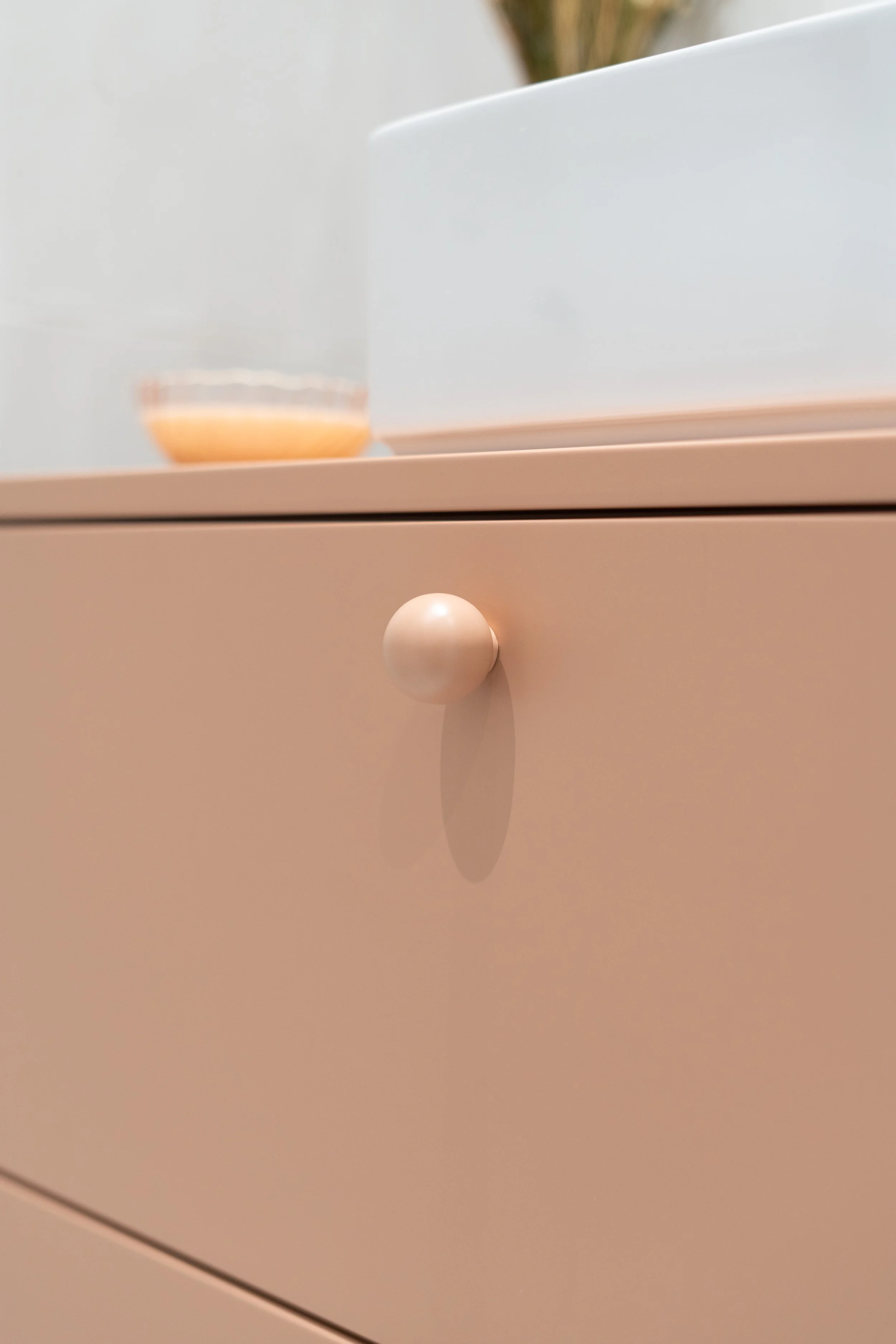 Une image d'une commode beige avec une poignée ronde, avec un verre et un plat sur le dessus.
