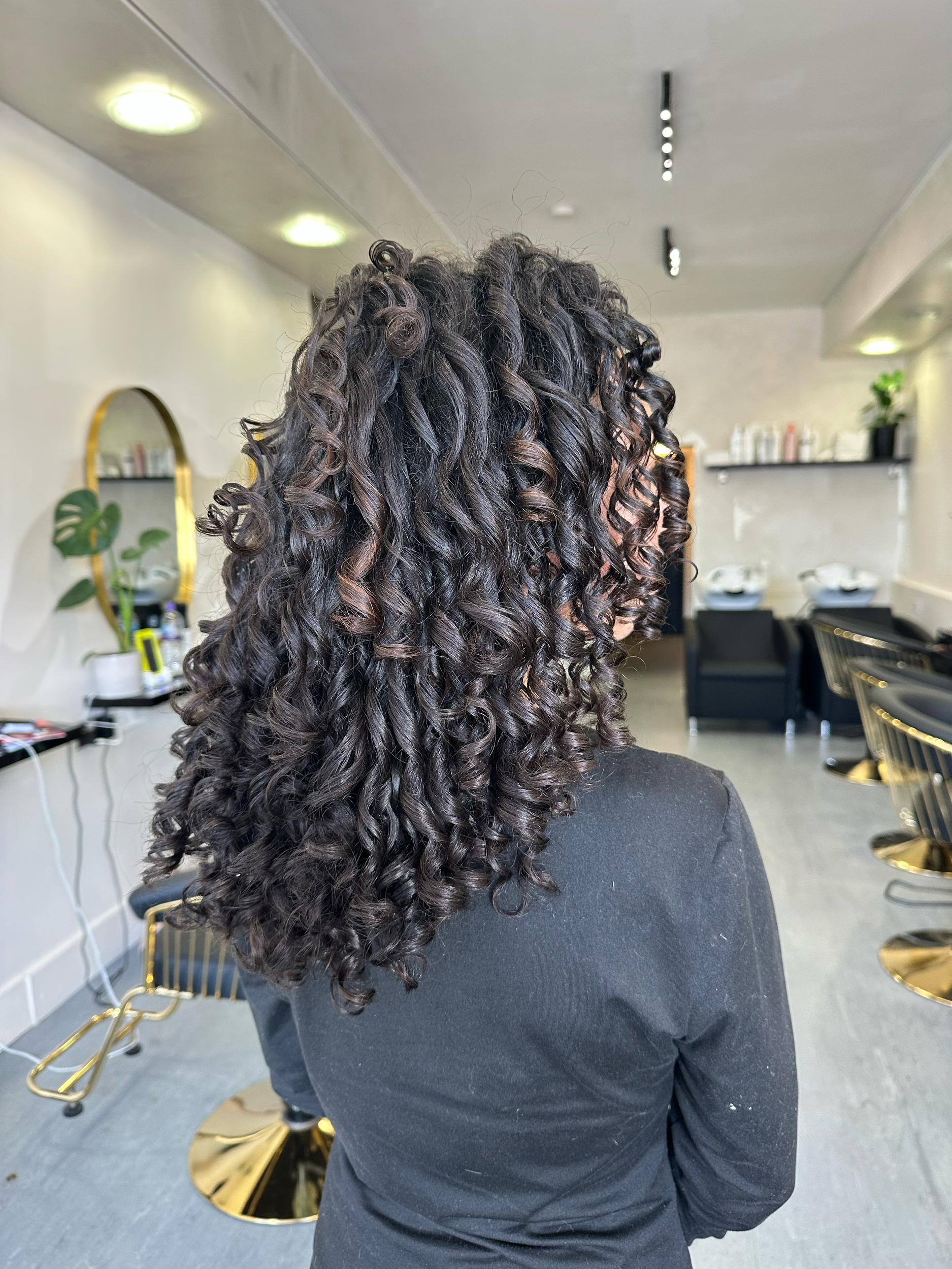 A woman with curly, dark hair standing in a hair salon.