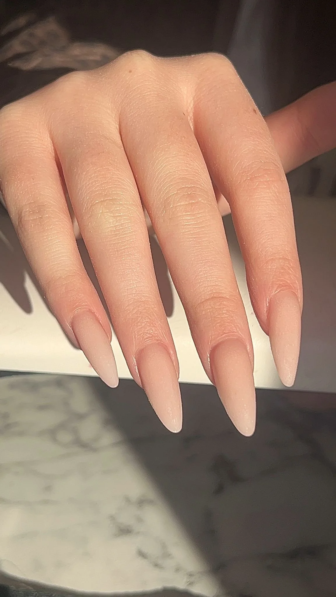 A close-up of a hand with long, pointed, nude-colored gel nails.