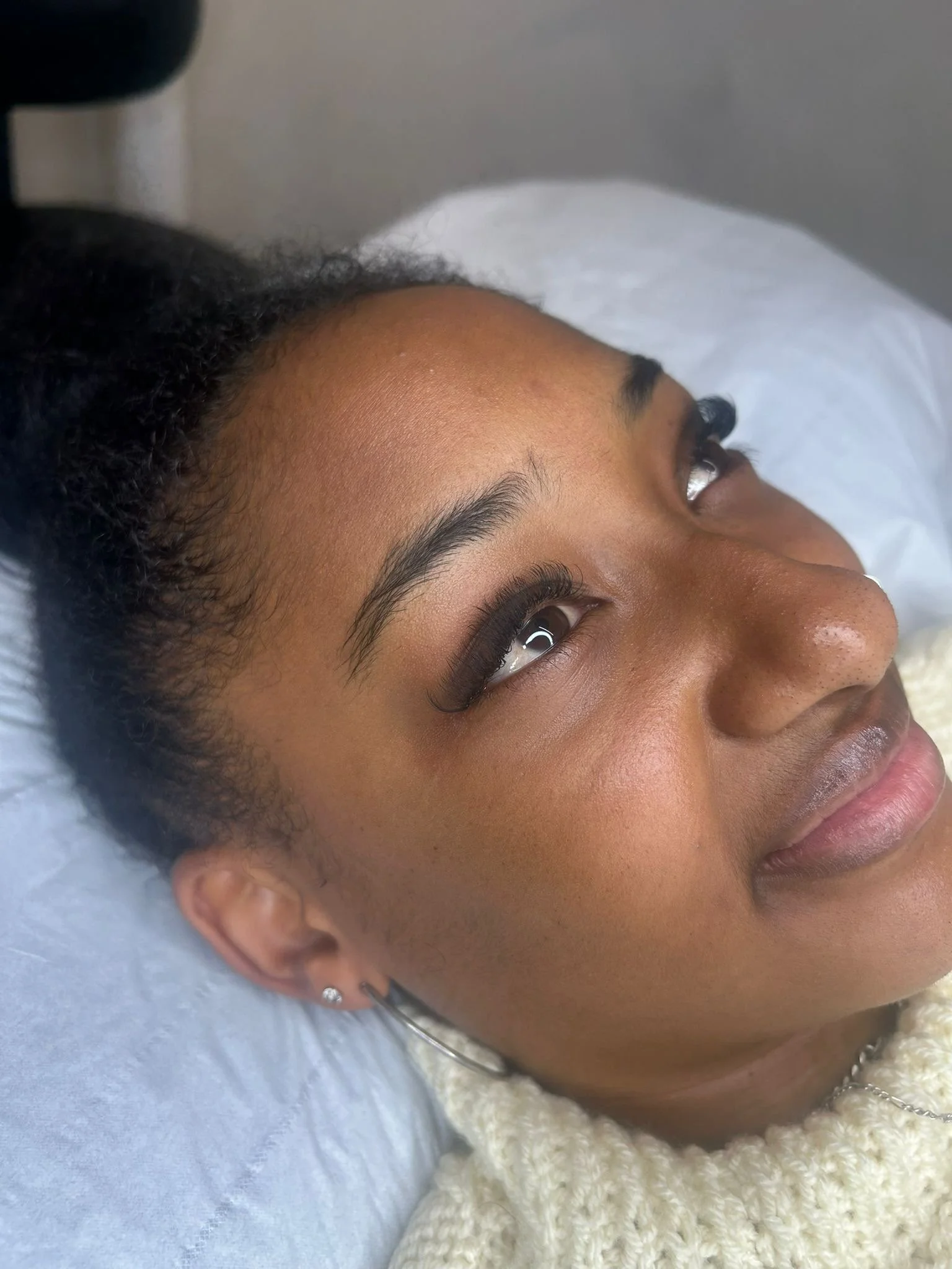 Close-up of a woman lying down with makeup and earrings, smiling slightly.