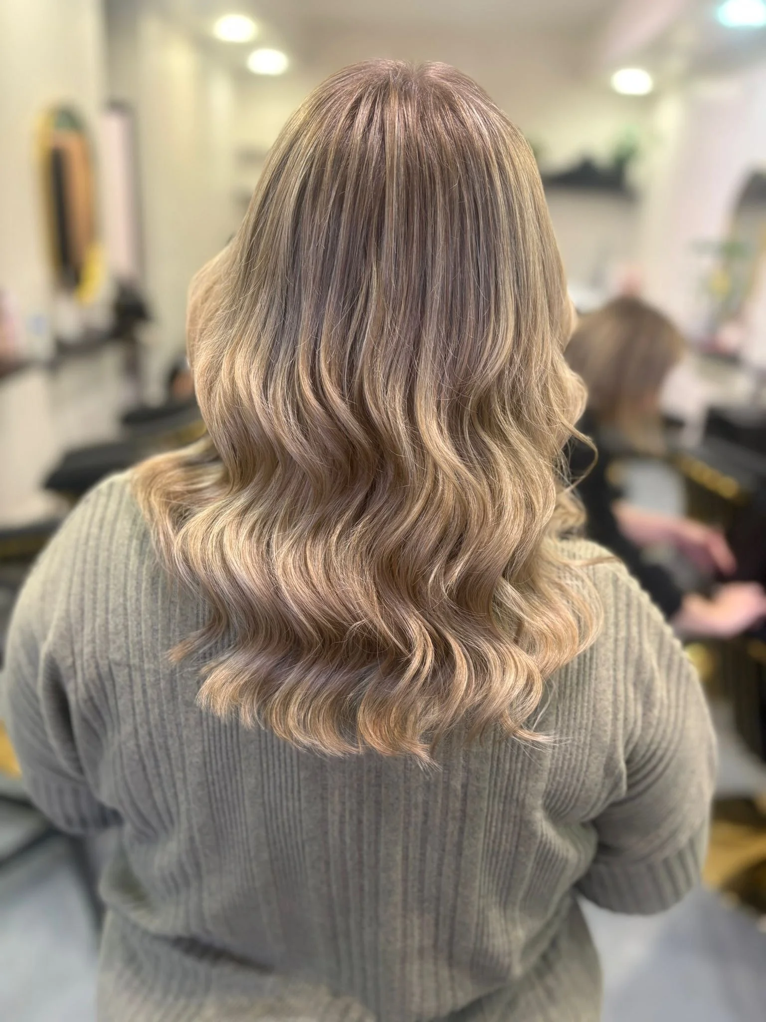 Back view of a woman with long, wavy, blonde hair in a salon.