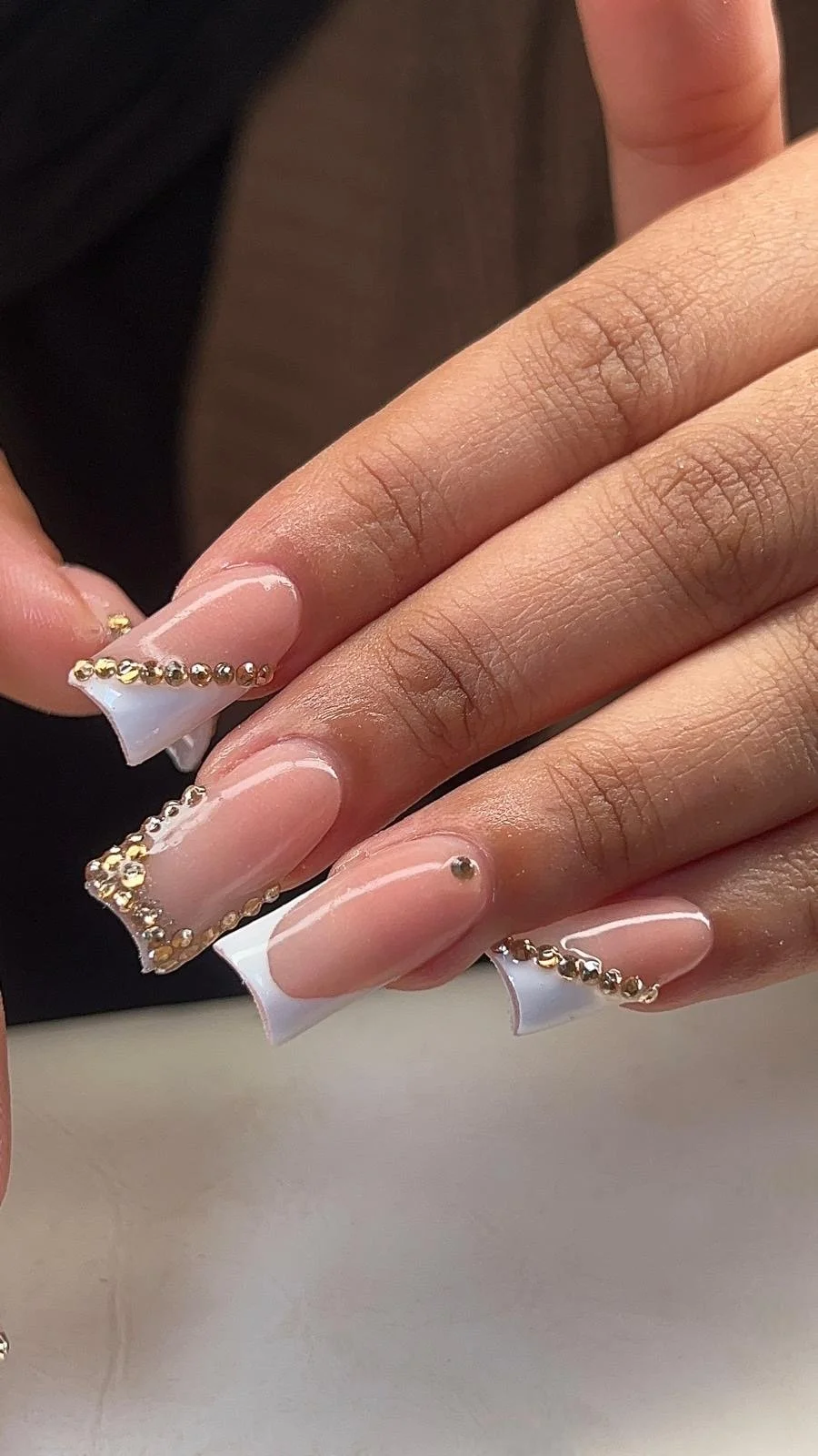 Close-up of manicured nails with clear polish, gold and silver beads, and white tips, held by fingers with natural skin tone.