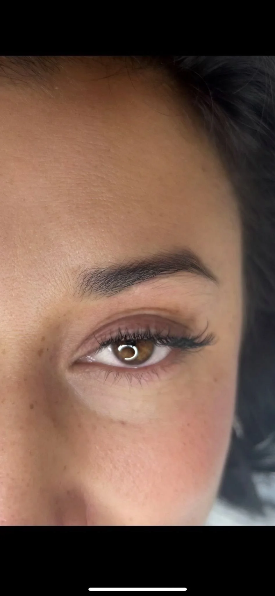 Close-up of a woman's face focusing on her eye, eyebrow, and surrounding skin, with brown eye color and natural makeup.