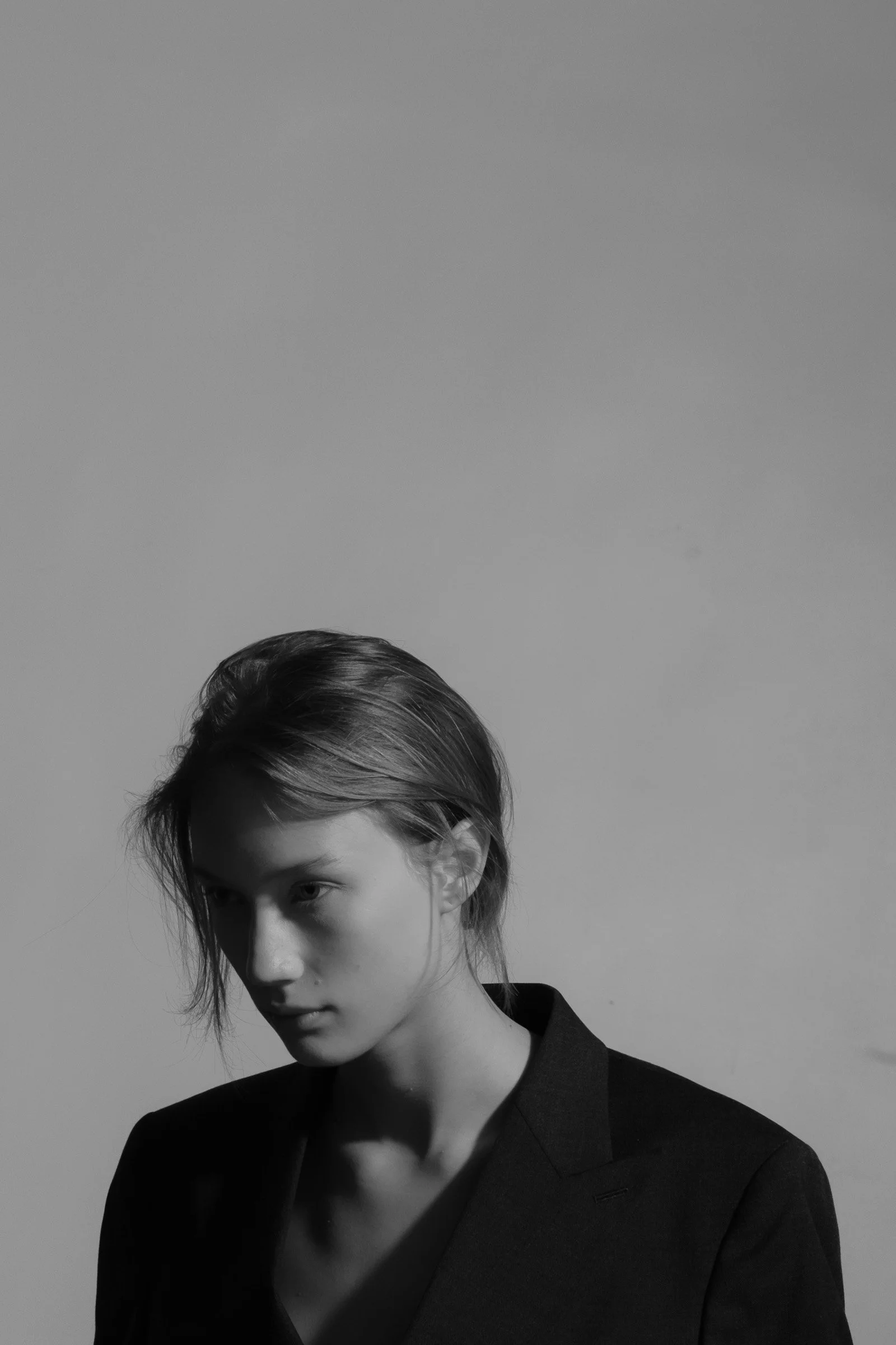 Portrait en noir et blanc d'une jeune femme aux cheveux courts, portant un blazer noir, regard contemplatif.