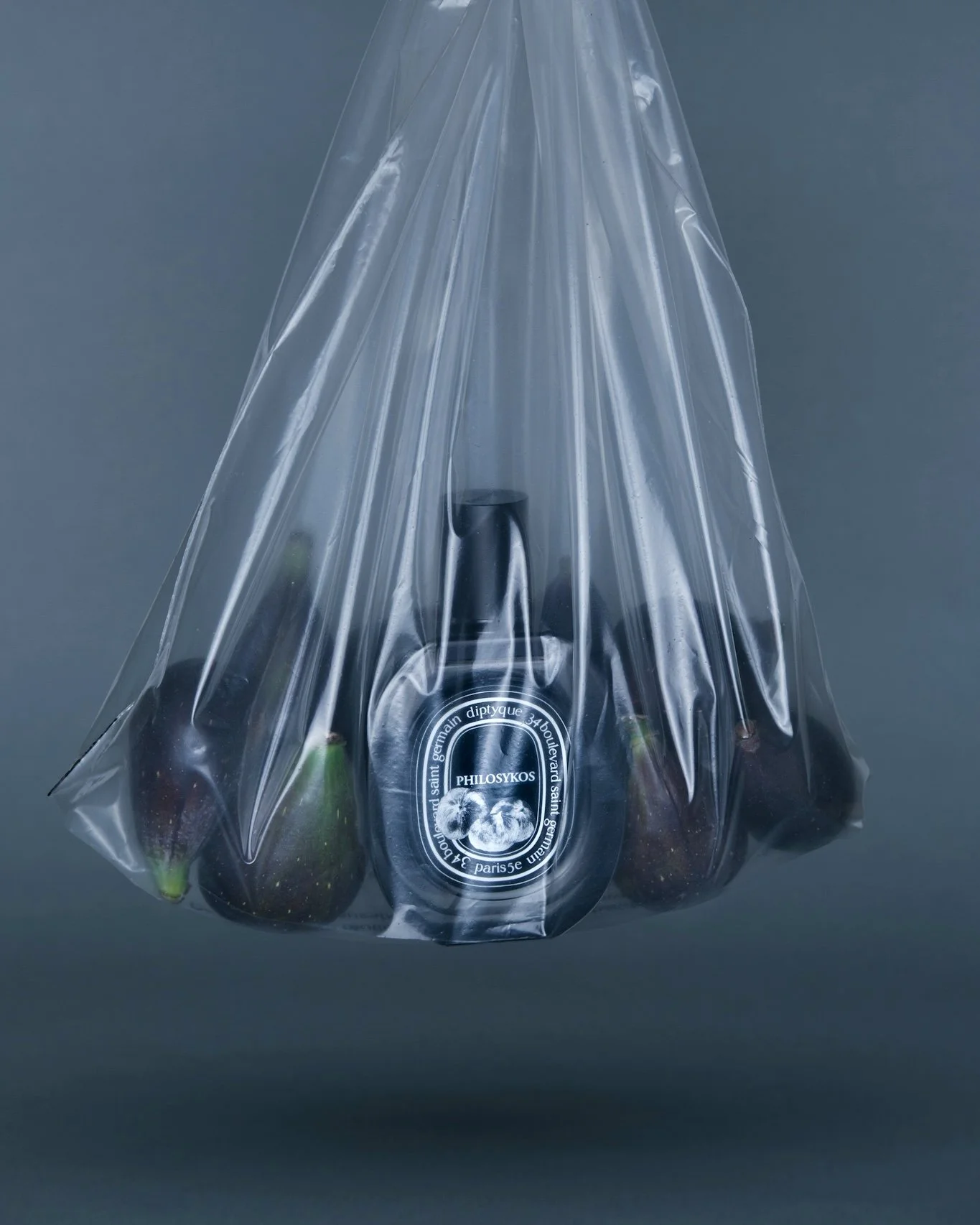 Un sac en plastique transparent contenant plusieurs figues et une bouteille de parfum Philosykos de Diptyque.