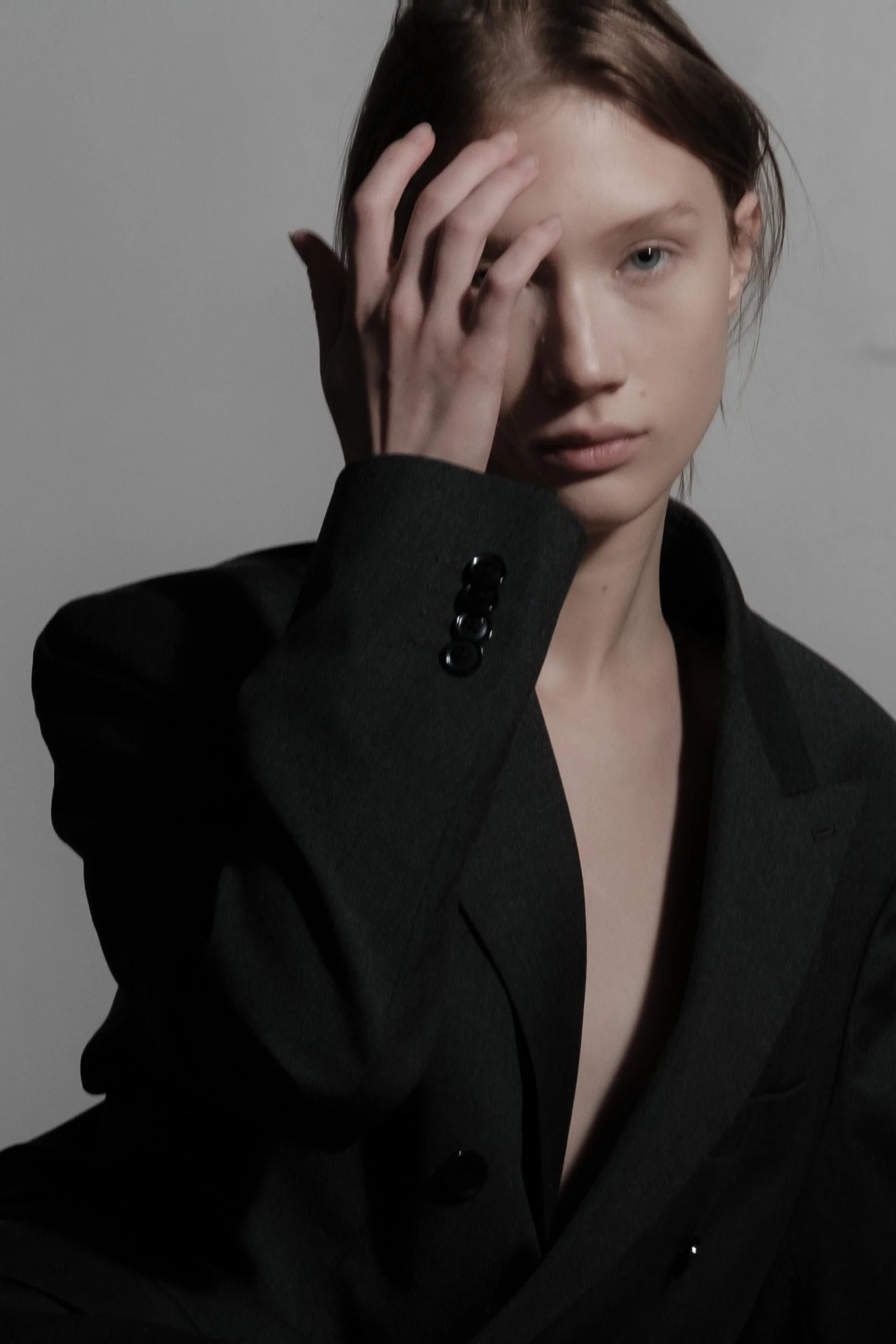 Jeune femme avec des cheveux bruns portant un blazer noir, tenant sa main devant son visage.