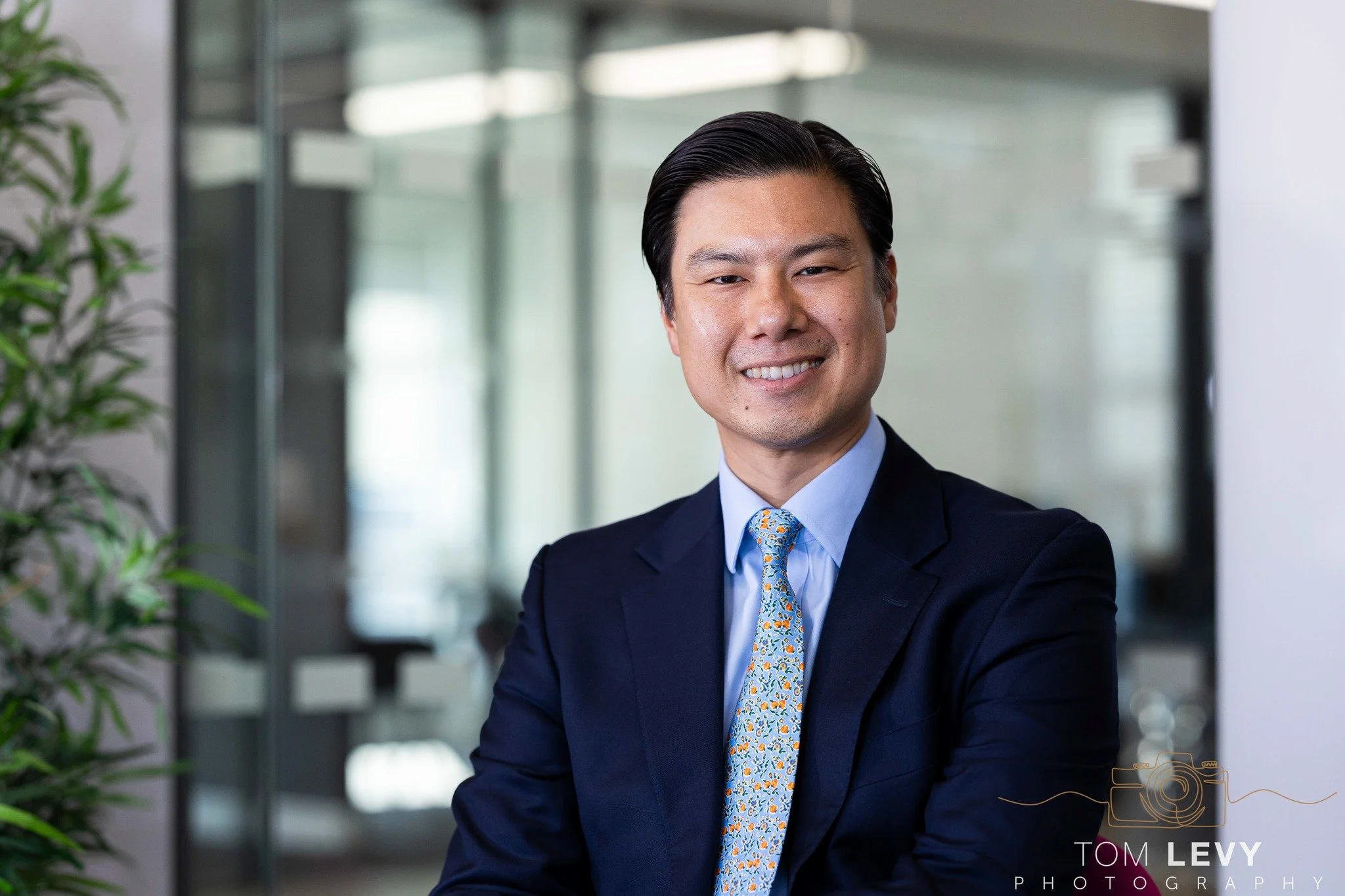 Smiling man in business suit standing in modern office environment with blurred background.