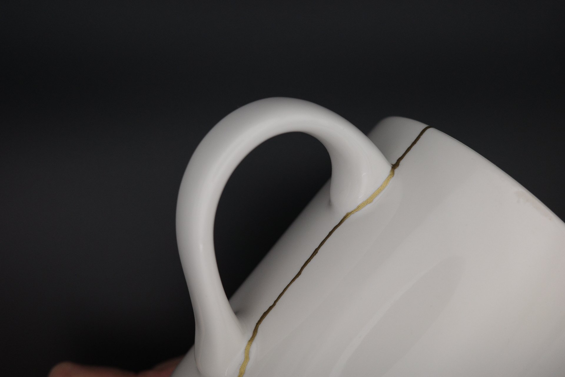 Close-up image of a white ceramic cup with crack repaired with kintsugi traditional techniques with brass.