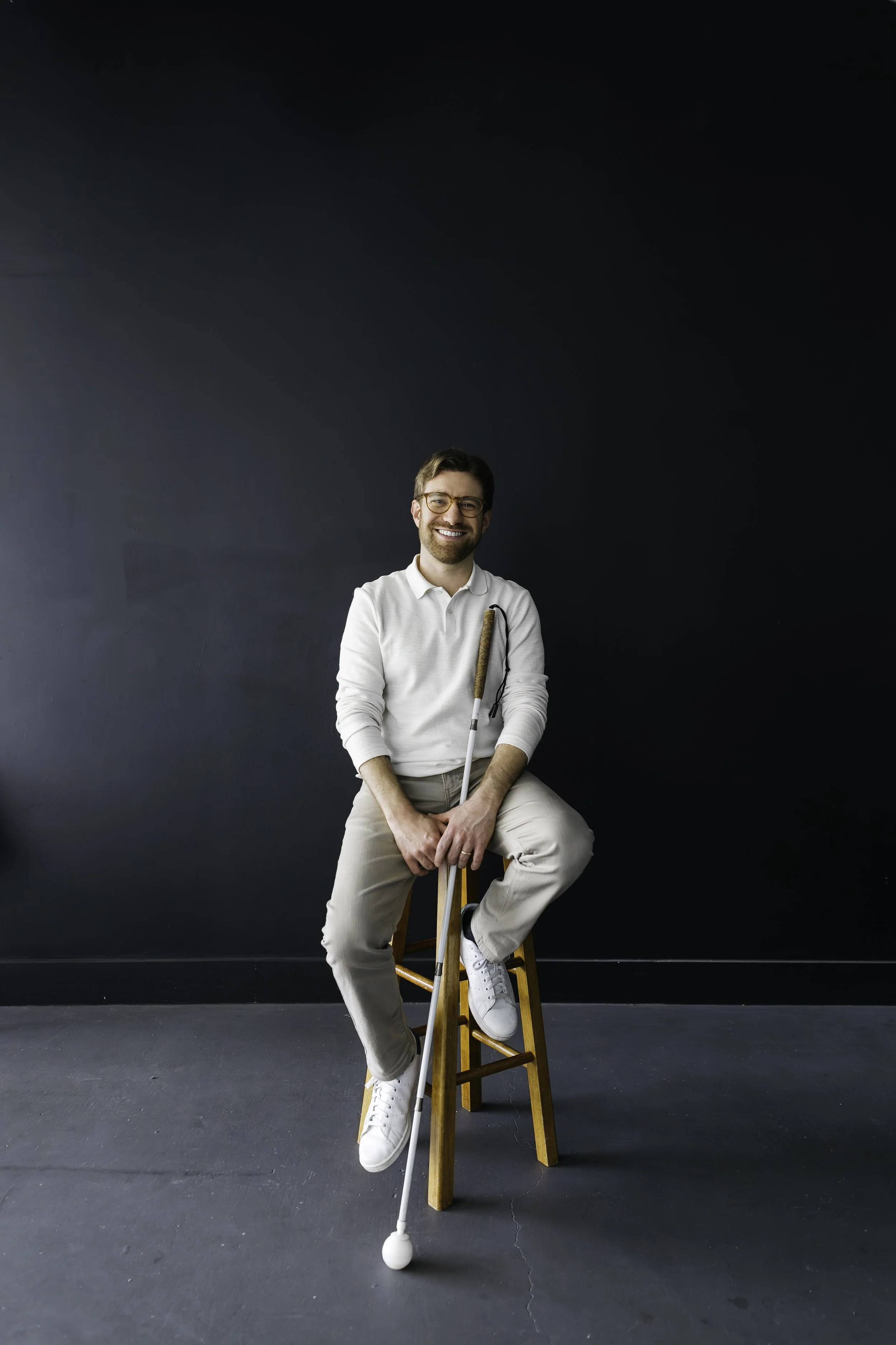 Charlie sitting on a stool in a black painted room while smiling and holding his cane.