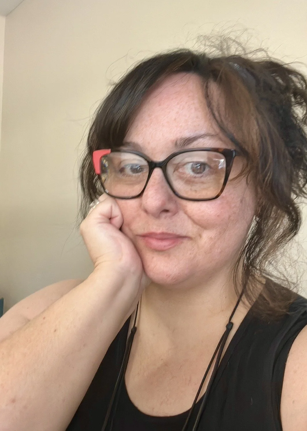 A woman with brown hair, glasses, and freckles resting her chin on her hand, looking into the camera.