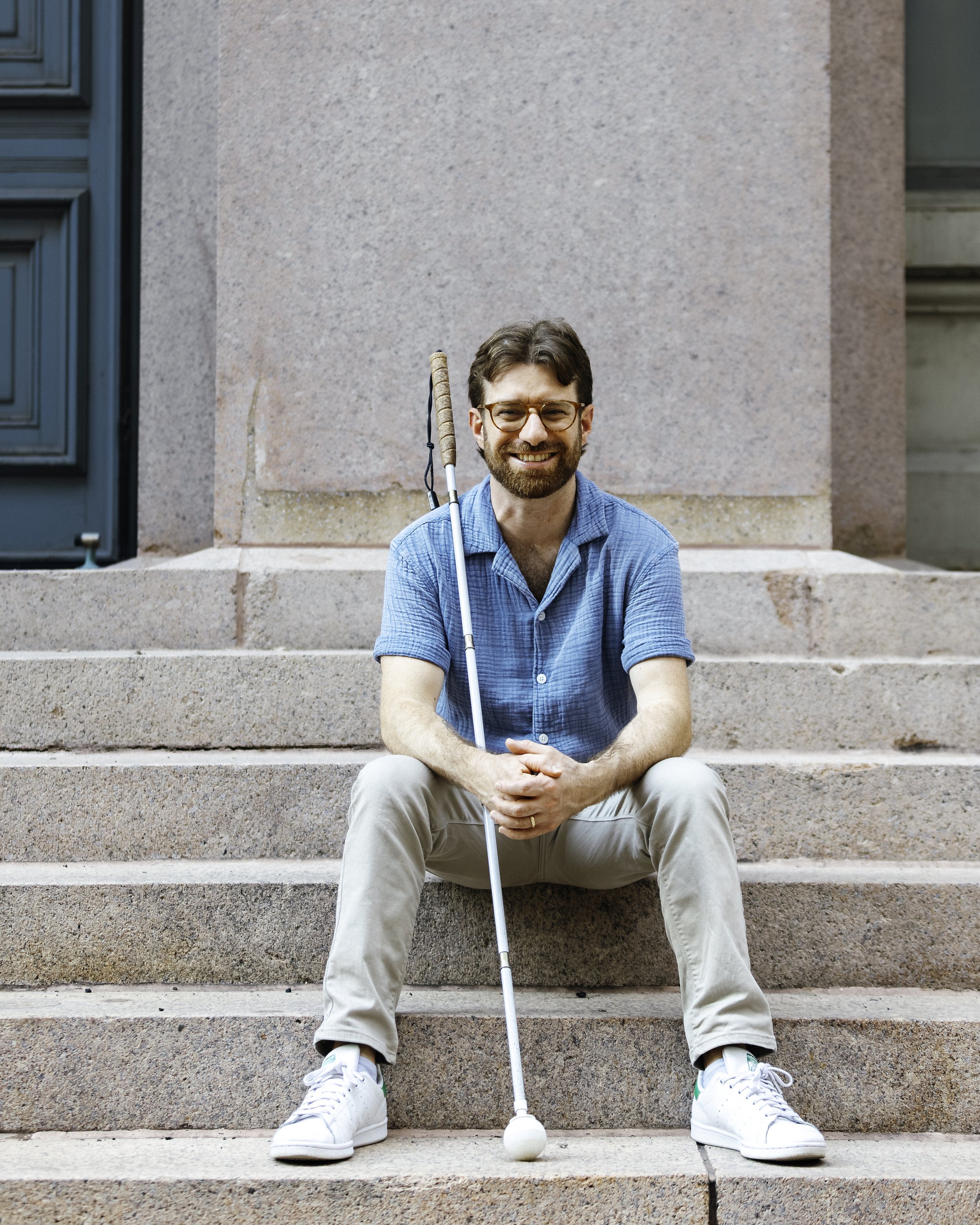 Charlie sitting outside on stone steps. He is smiling and holding his cane.