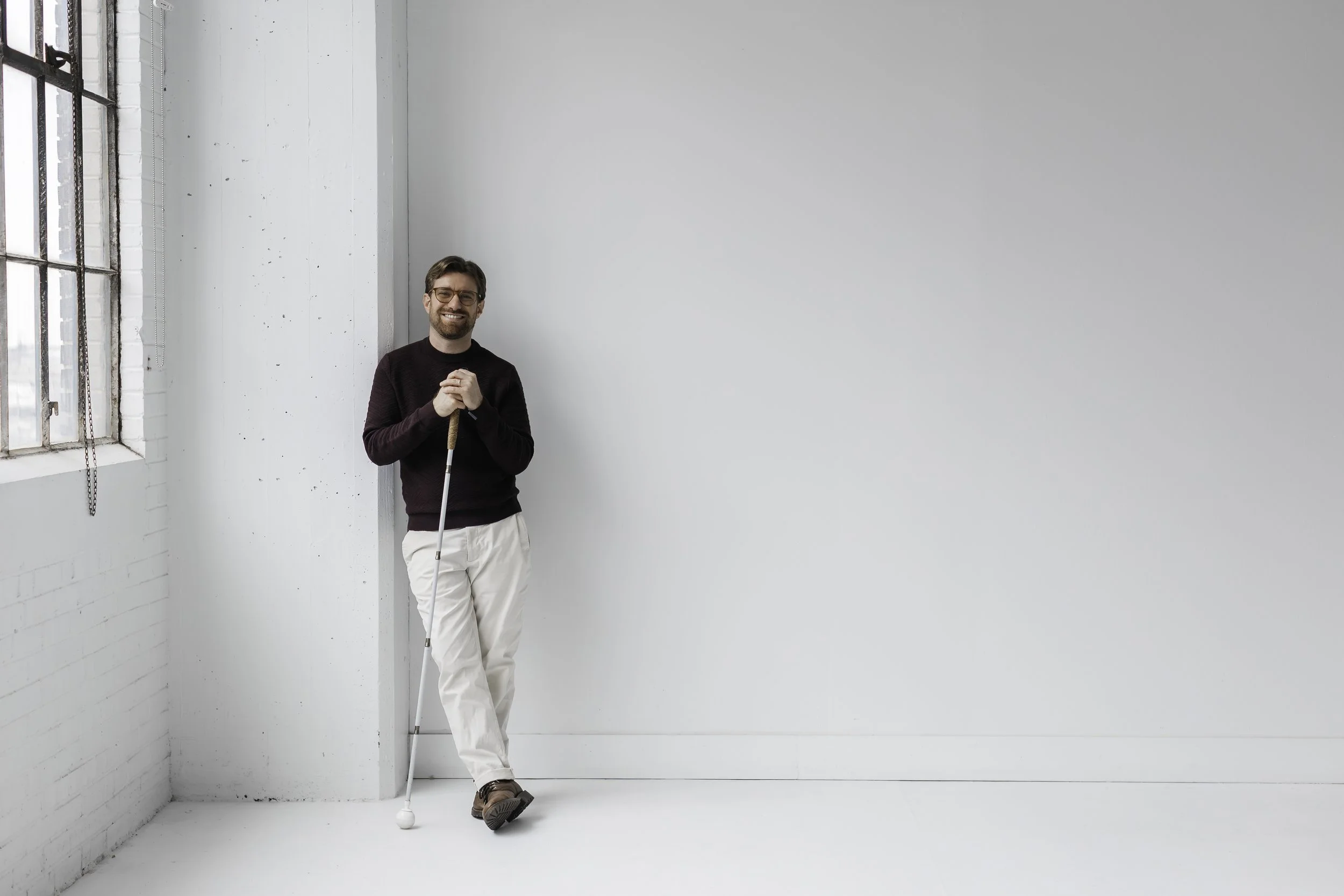 Charlie standing and smiling in a white-painted room. He is holding his cane. 