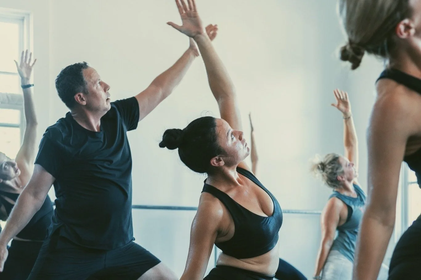 People participating in a yoga or exercise class, performing high-reaching stretches in a bright room.