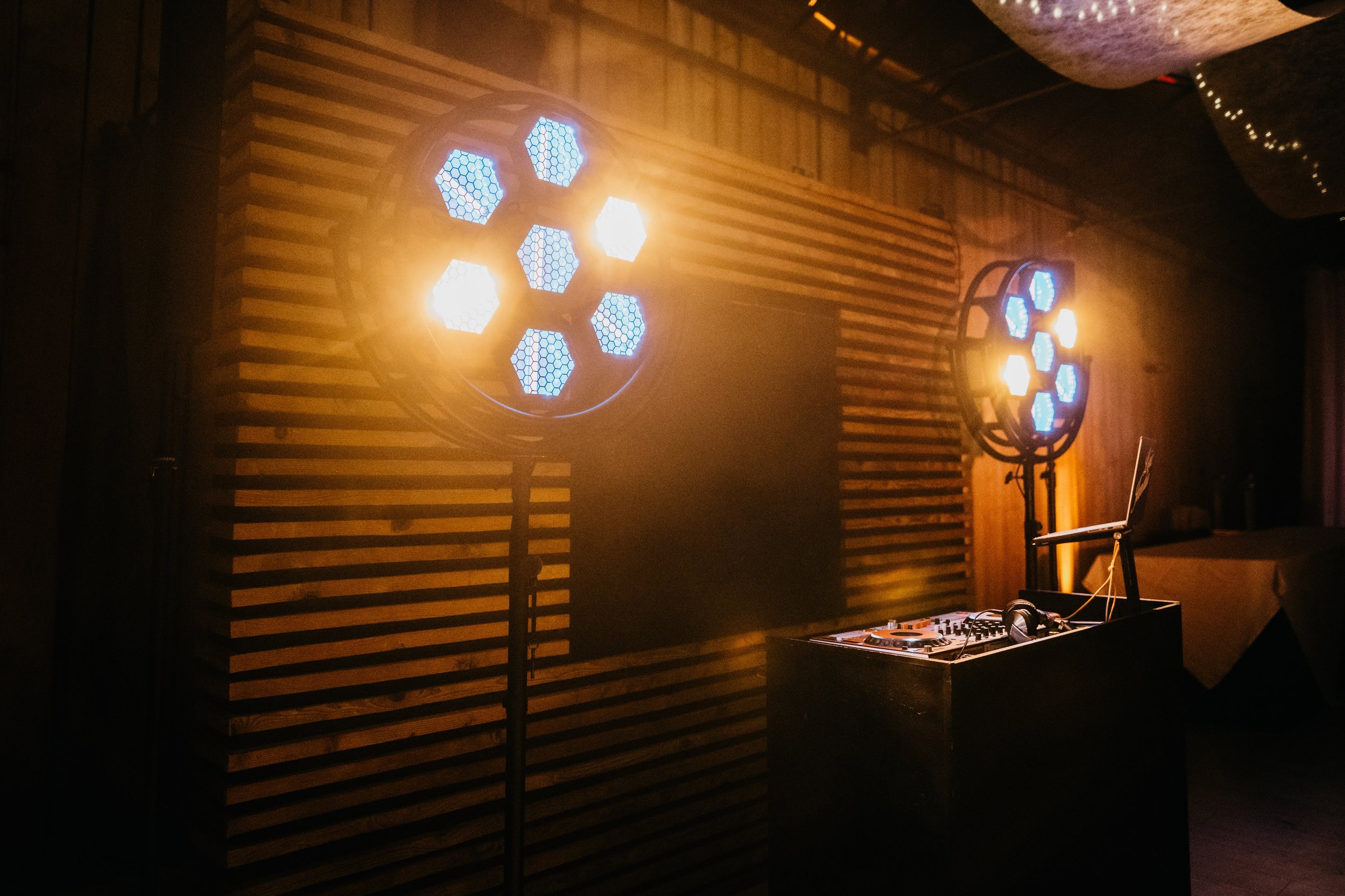 Eclairage de discothèque avec projecteurs bleus et jaunes, panneau en bois derrière, table de mixage avec casque et ordinateur portable.