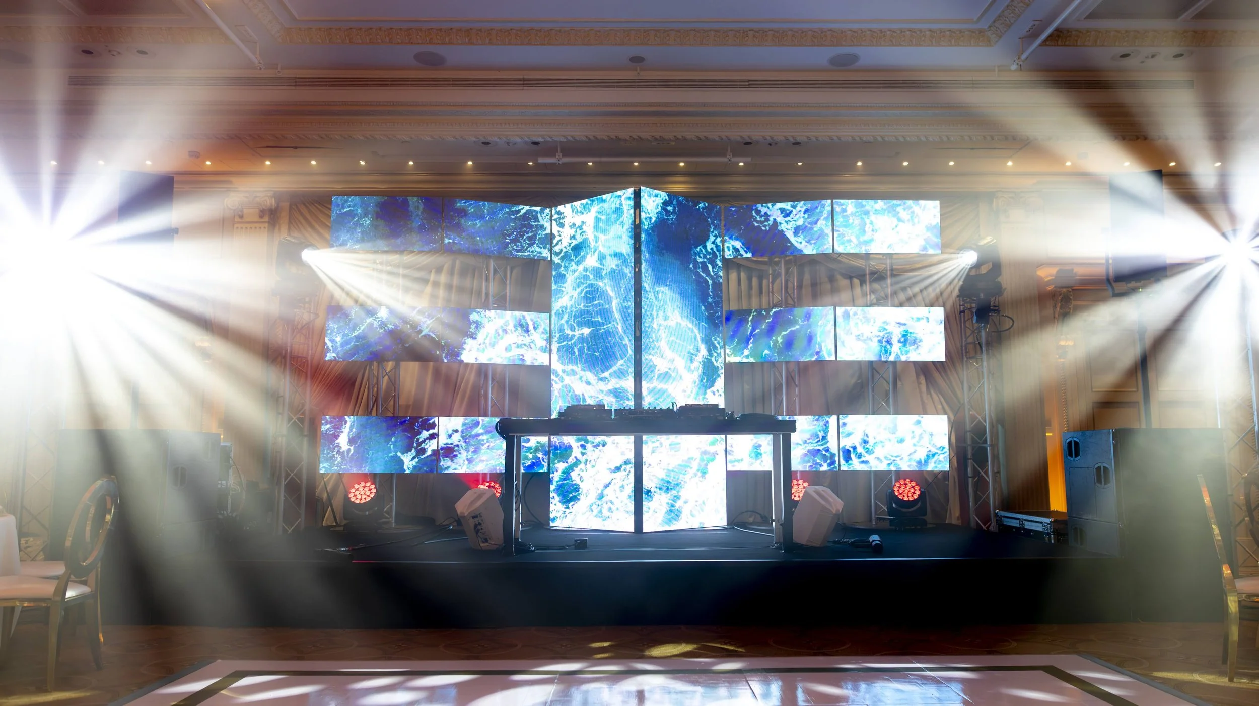 Une scène de fête ou de concert avec un grand écran lumineux affichant des images d'eau en mouvement, un DJ set avec une table de mixage, et des éclairages spectaculaires créant des rayons lumineux.