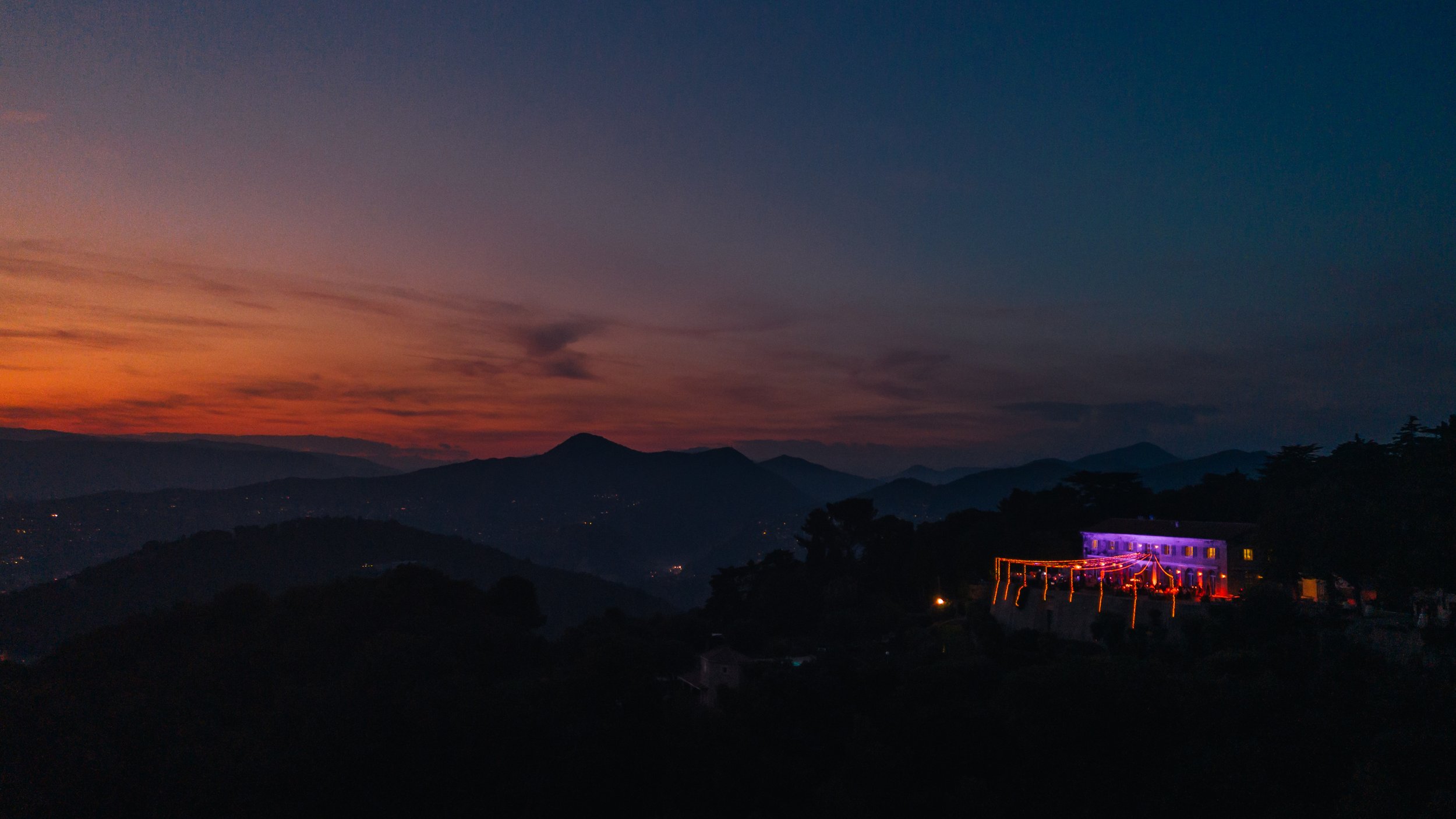 Paysage au coucher du soleil avec des montagnes et un bâtiment illuminé.