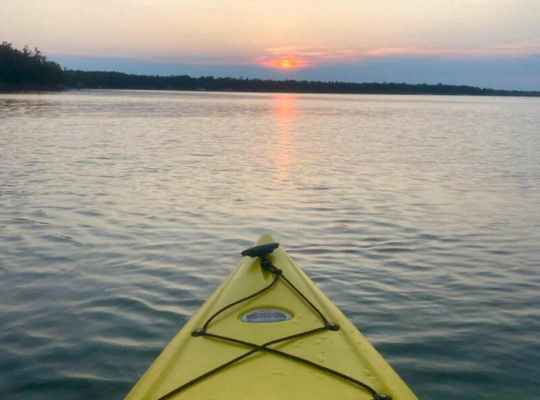 A yellow kayak floating on calm water during a sunset.