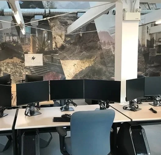 Office workspace with six monitors, a blue chair, and a window with mountain and canyon scenery in the background.