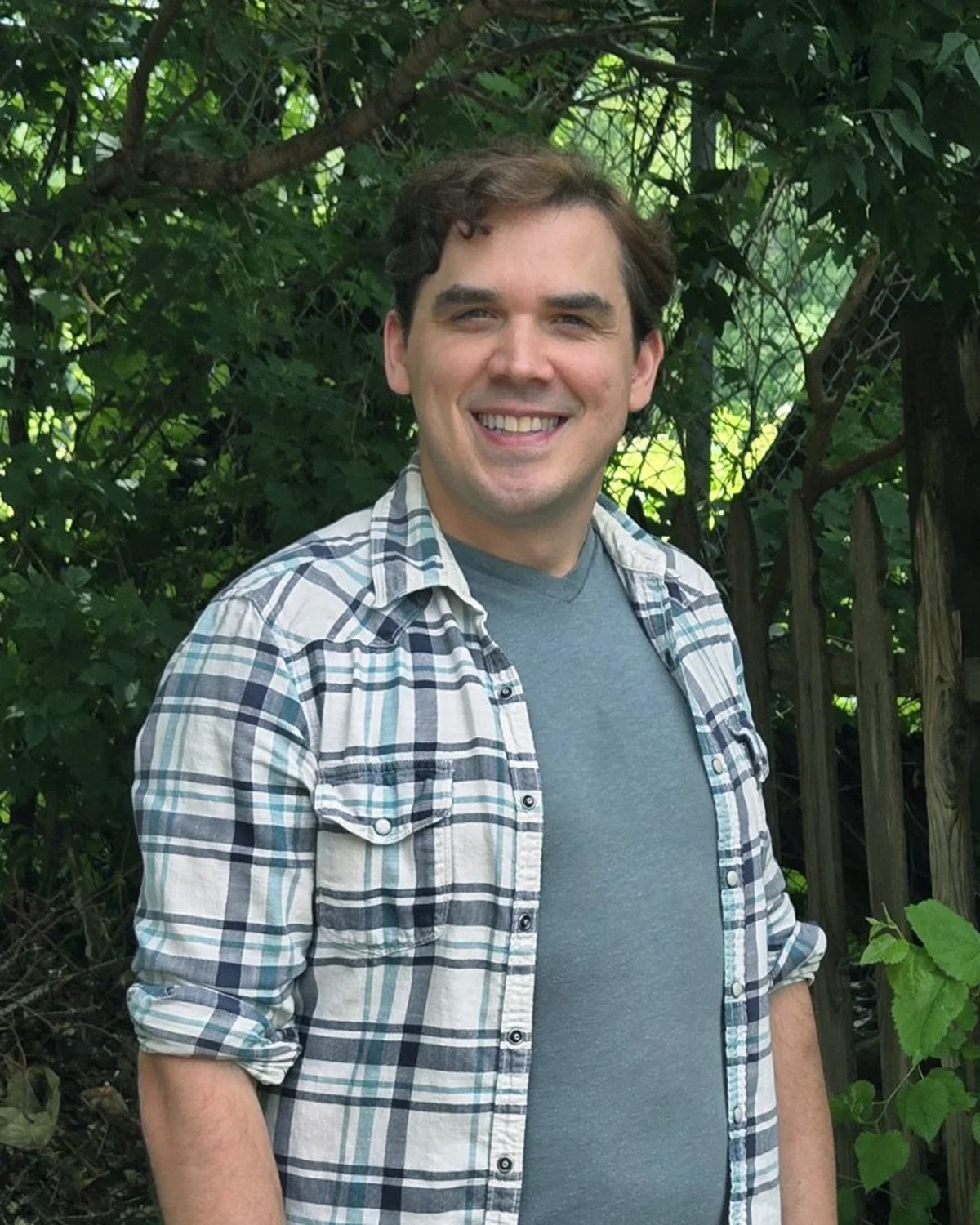 Picture of man in plaid shirt posing in front of wooded forest