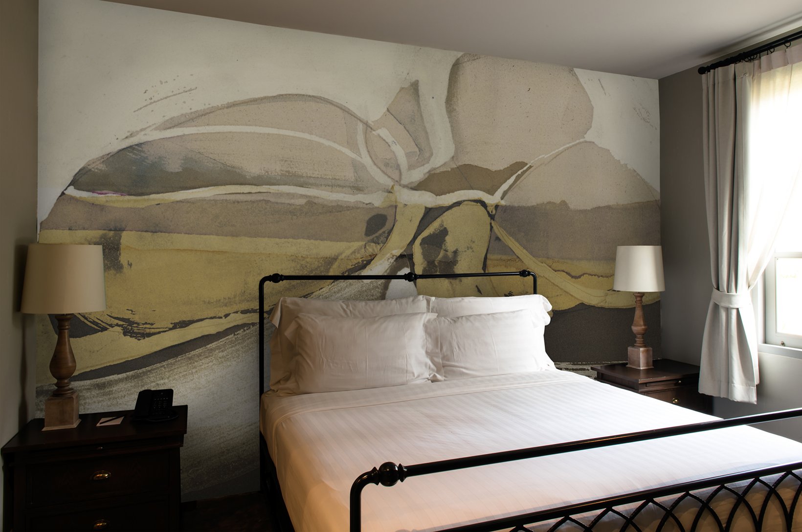 Bedroom with a large abstract mural of a butterfly on the wall behind the bed, two bedside tables with lamps, and a window with curtains.