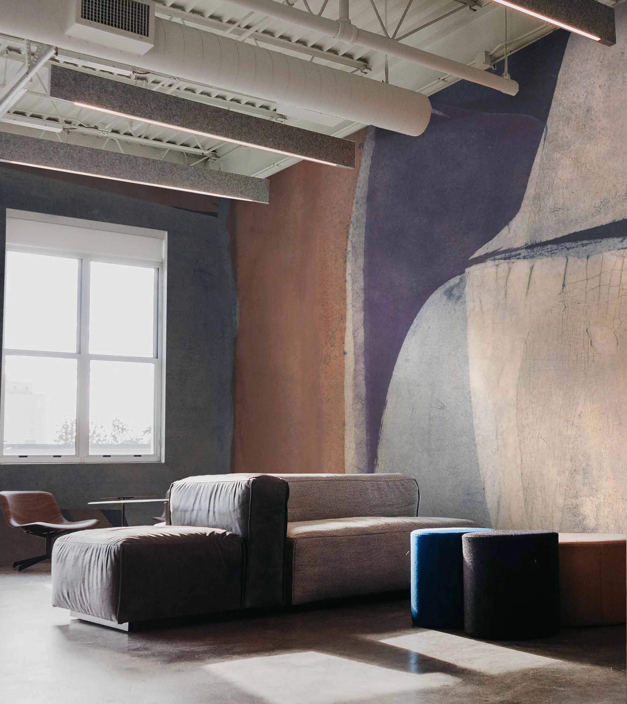 Modern interior space with large window, comfortable couches, colorful pouf, and abstract carpet design.