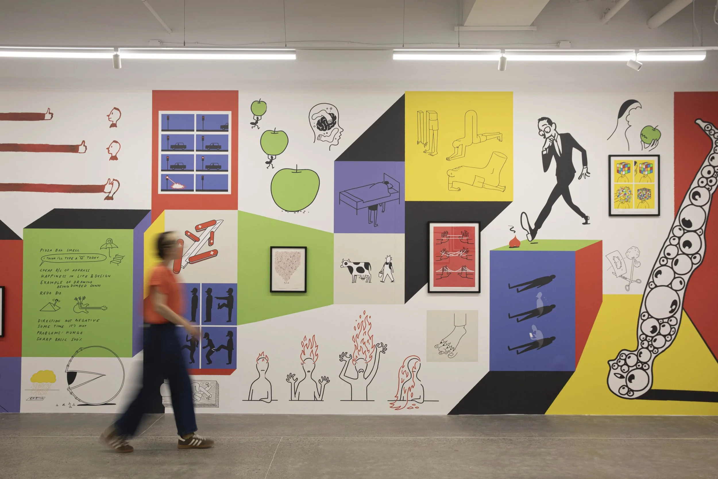 A person walking in front of a colorful mural on a wall, featuring various abstract drawings, illustrations, and text.