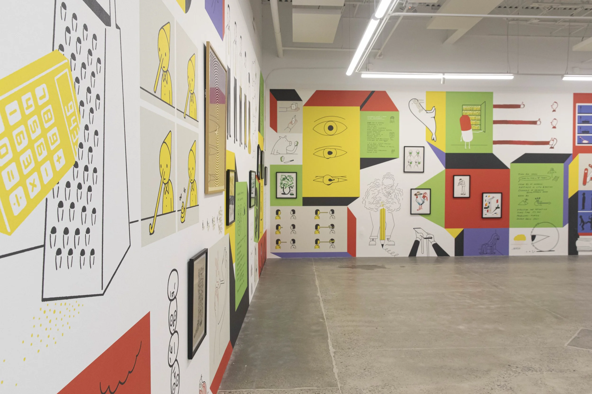 Colorful art exhibit with various illustrations and framed artworks on the wall, including images of eyes, animals, and abstract designs, in a spacious gallery with concrete flooring.